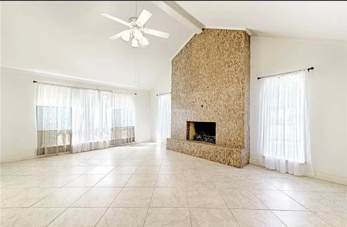 Vaulted ceiling featuring a ceiling fan, a large stone-clad fireplace, and tile flooring