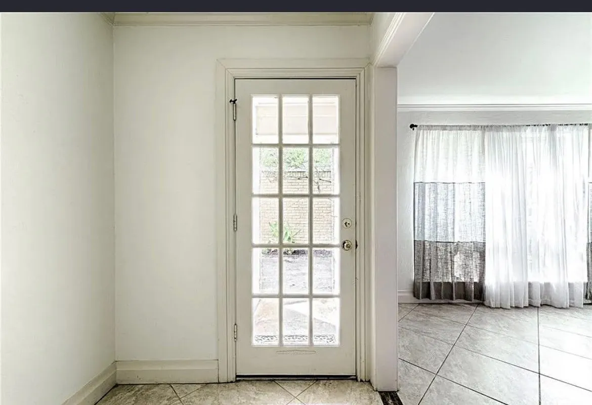 French paneled glass door with white trim, leading to a room featuring large windows with sheer curtains, and large-format tile flooring