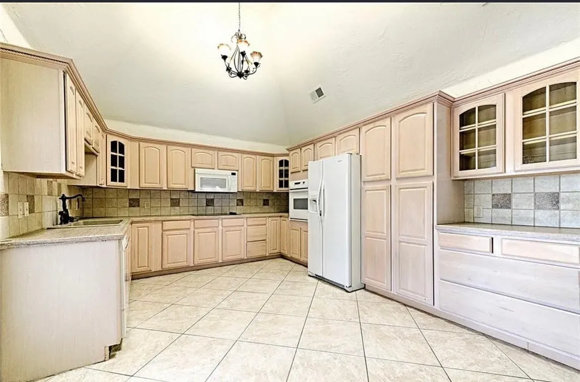Spacious kitchen featuring light wood cabinetry with glass-front upper cabinets, tile backsplash, ceramic tile flooring, and stainless steel appliances including a side-by-side refrigerator and white range