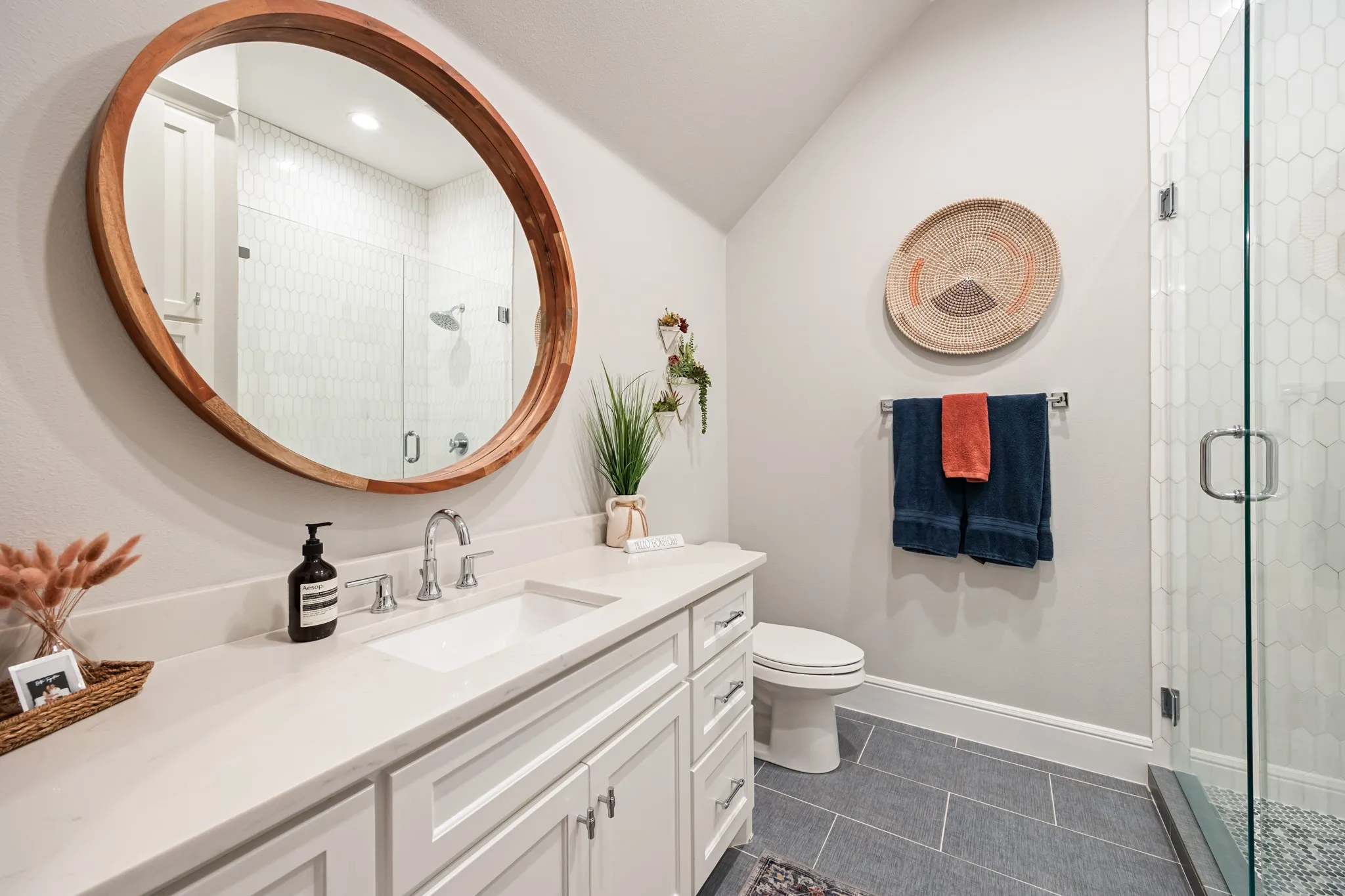 En-suite bath finished with a warm wood-framed mirror and glass shower.