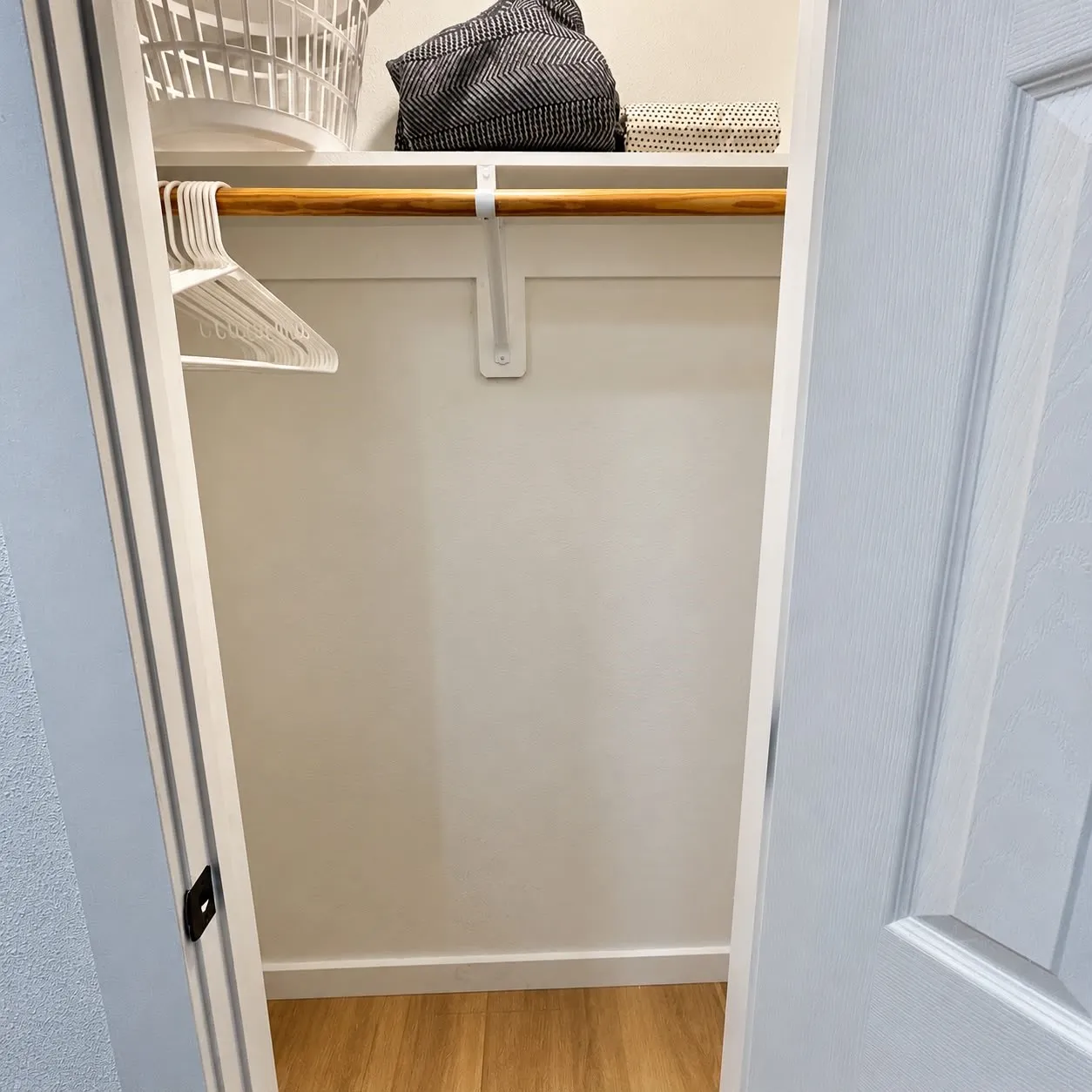 Integrated shelving unit with a wooden hanging rod, light-toned wood-finish flooring, and a paneled door
