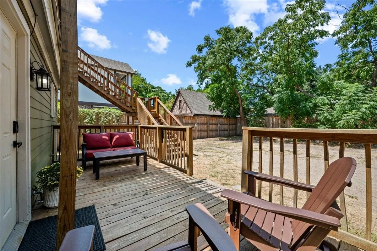 Expansive wood deck with a built-in railing, exterior wall lantern, and a multi-level wooden staircase