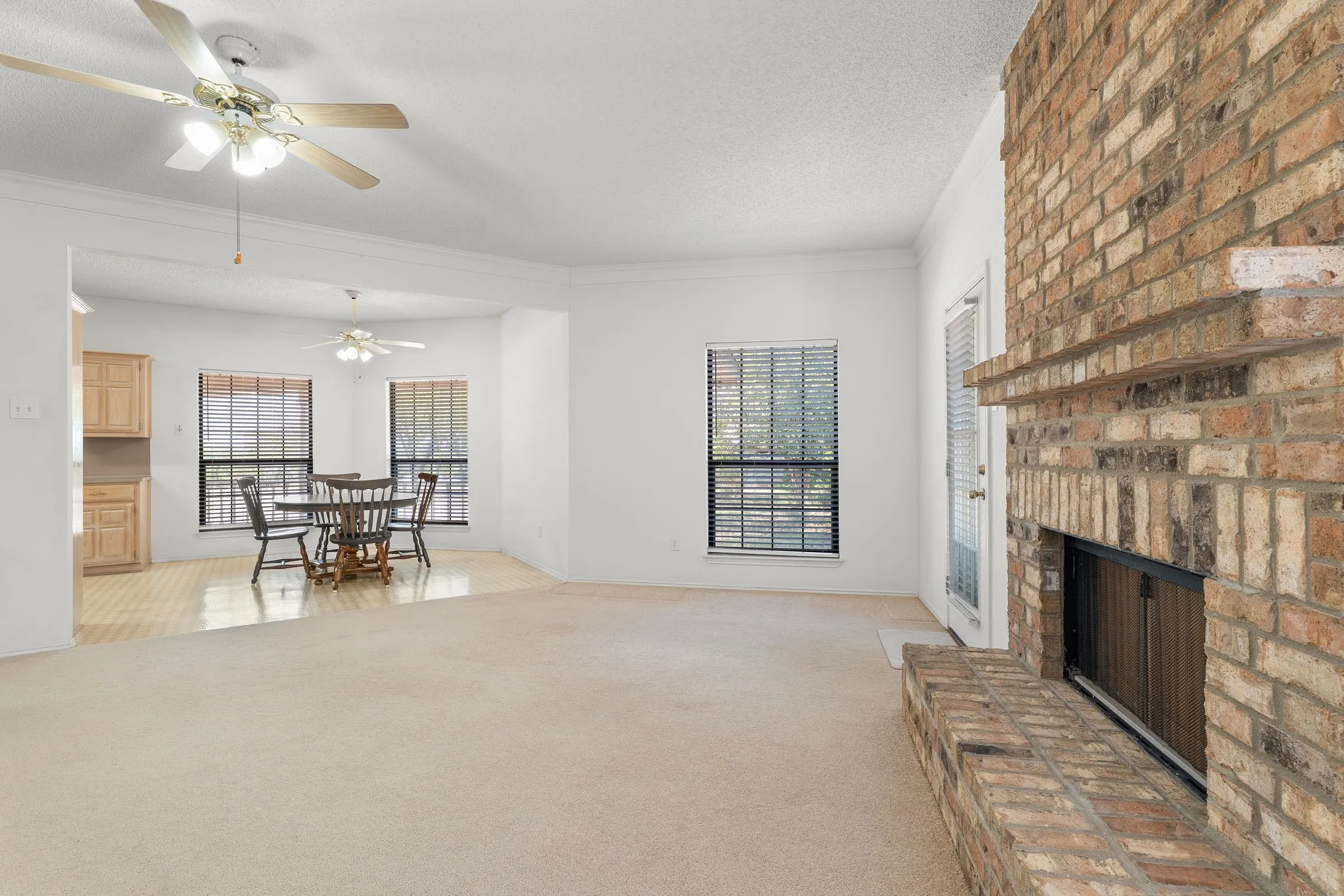 Brick-faced fireplace with a hearth, carpeted flooring, and a ceiling fan