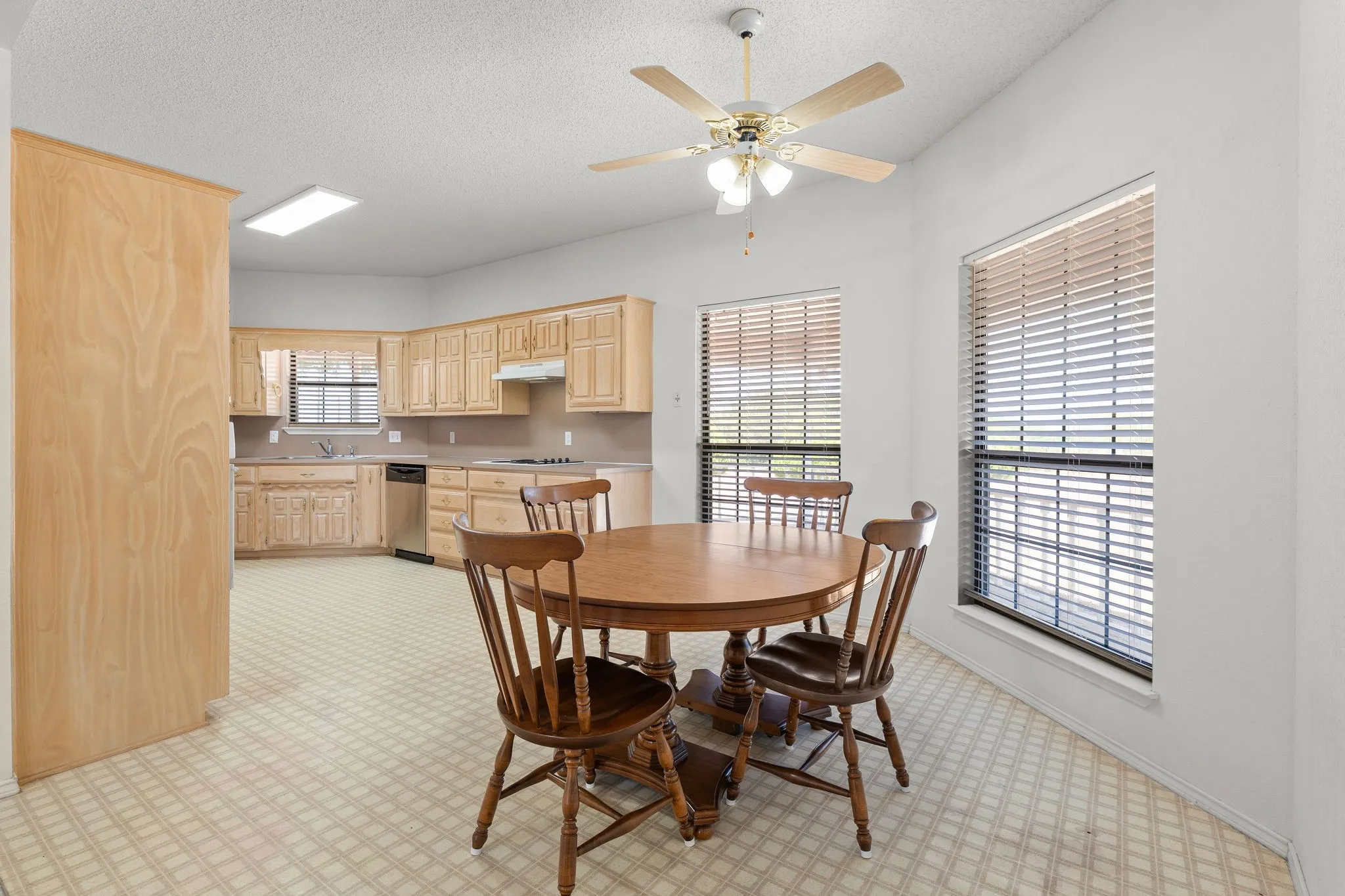 Kitchen with light wood cabinetry, stainless steel dishwasher, and patterned flooring