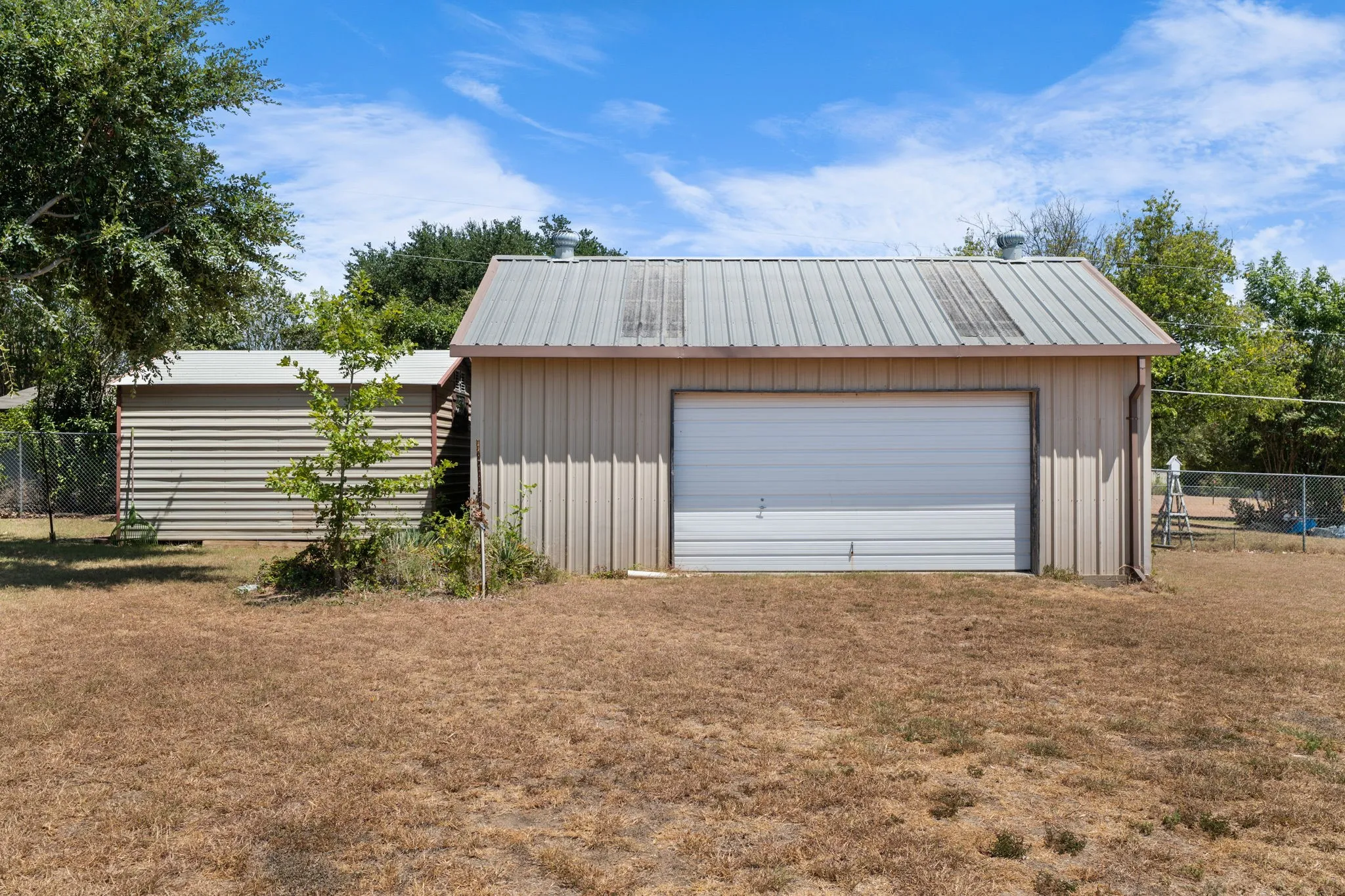 Detached garage with metal siding and a roll-up door, complemented by an additional storage structure featuring horizontal siding
