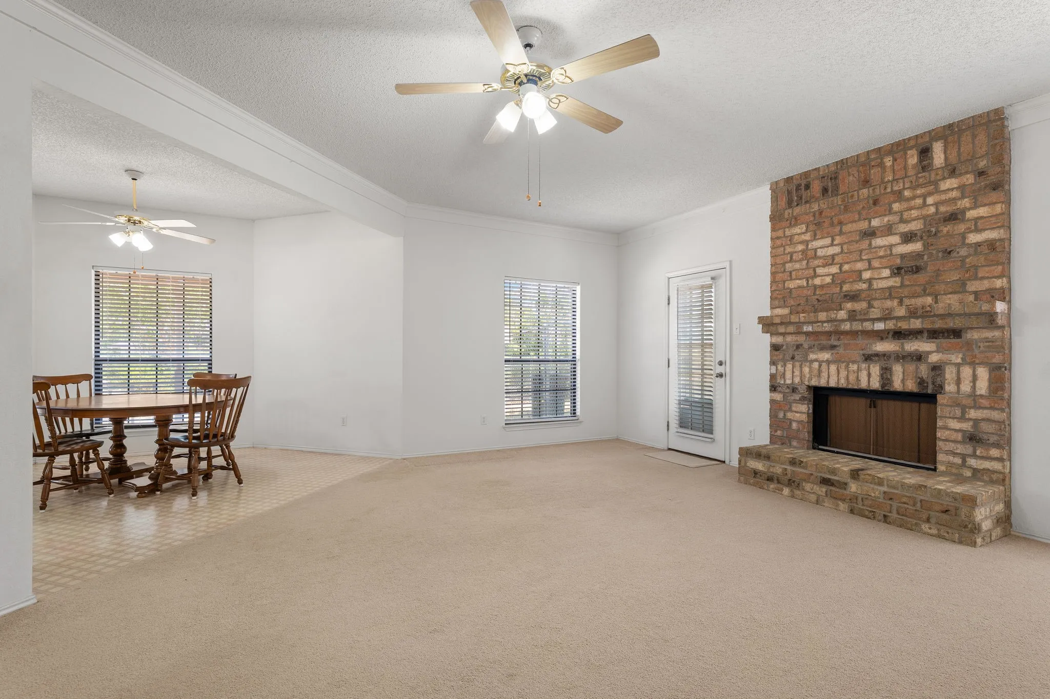Brick-surround fireplace with hearth, multiple windows with blinds, and ceiling fans