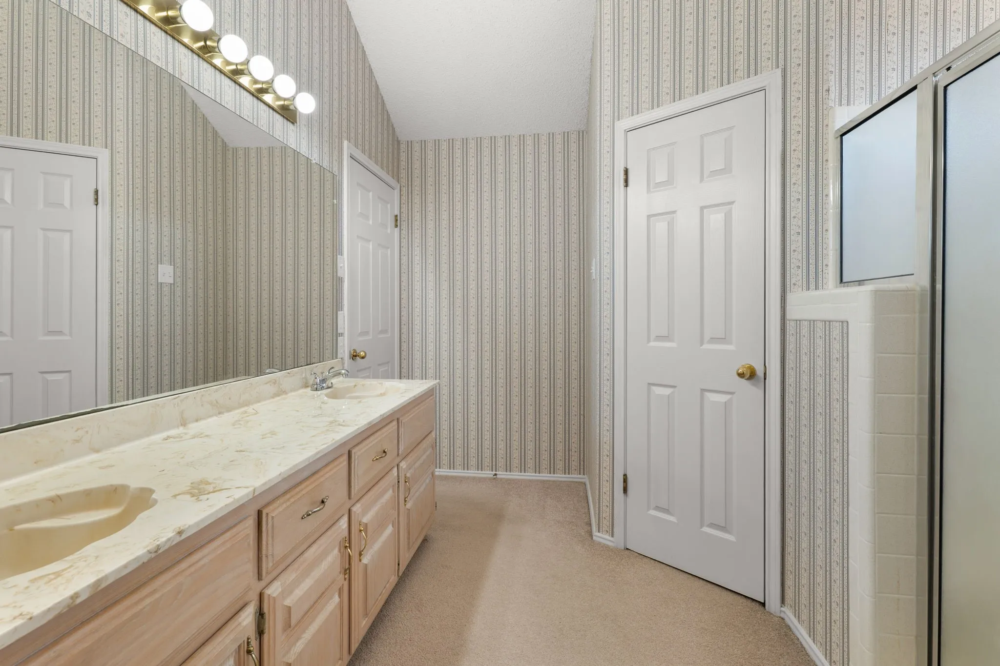 Dual-sink vanity with a light-toned countertop, extensive wall-mounted mirror, and overhead vanity lighting