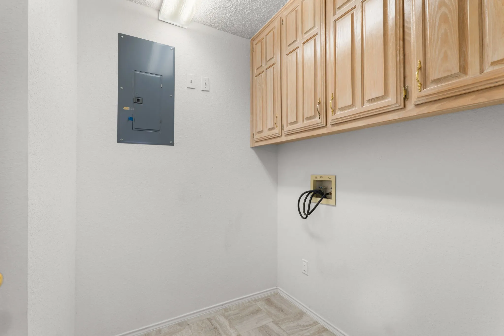 Overhead wood-finish cabinetry, electrical panel, and light-toned flooring