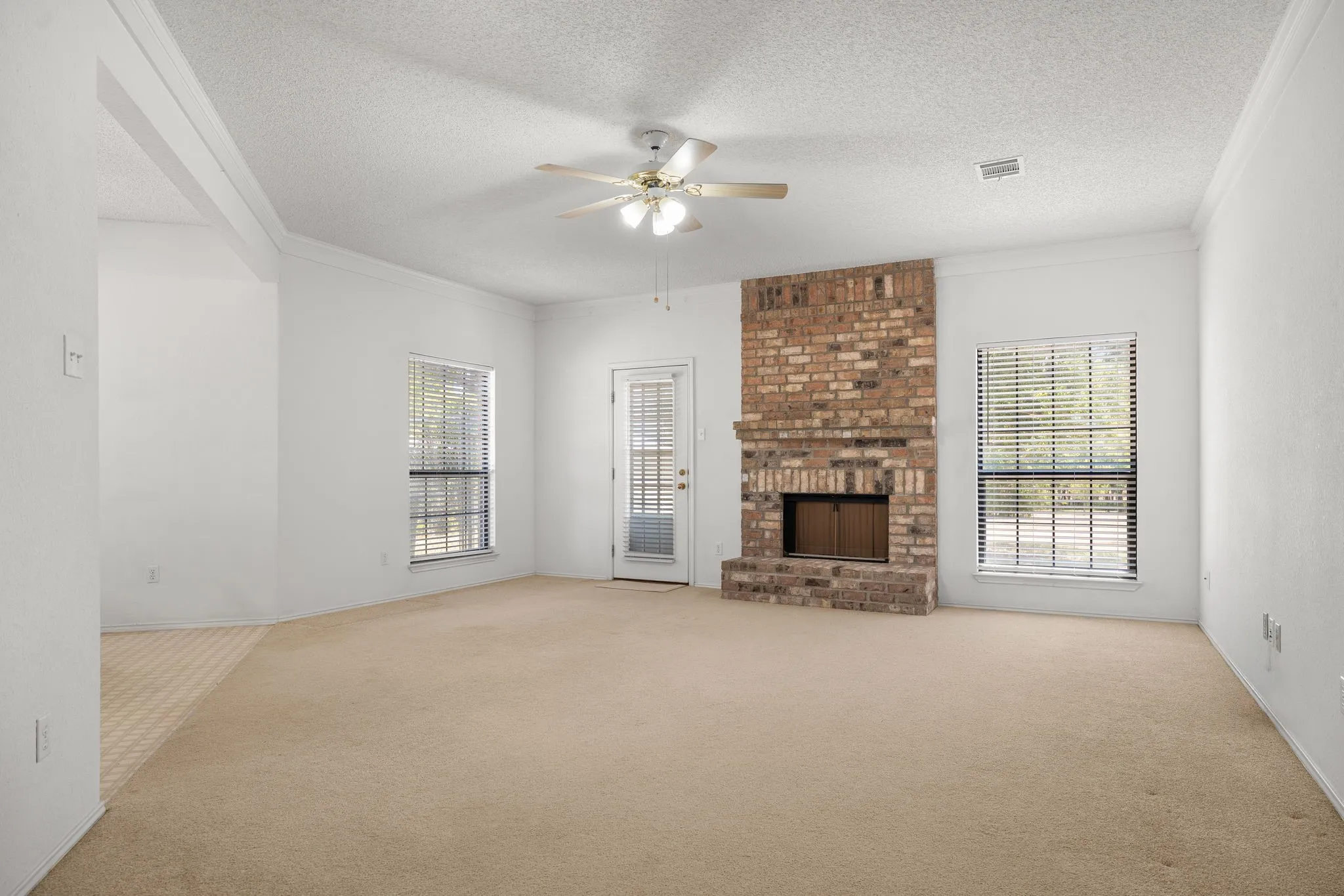 Spacious living area featuring a brick fireplace, ceiling fan, and multiple windows with blinds