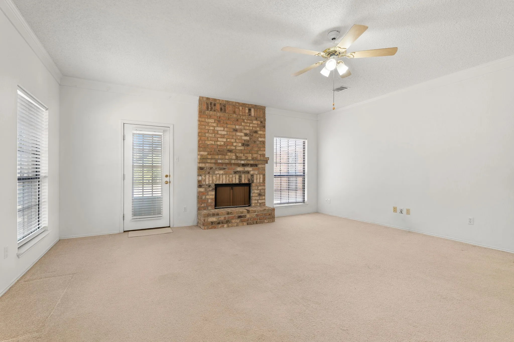 Brick-faced fireplace, large windows, ceiling fan, and crown molding