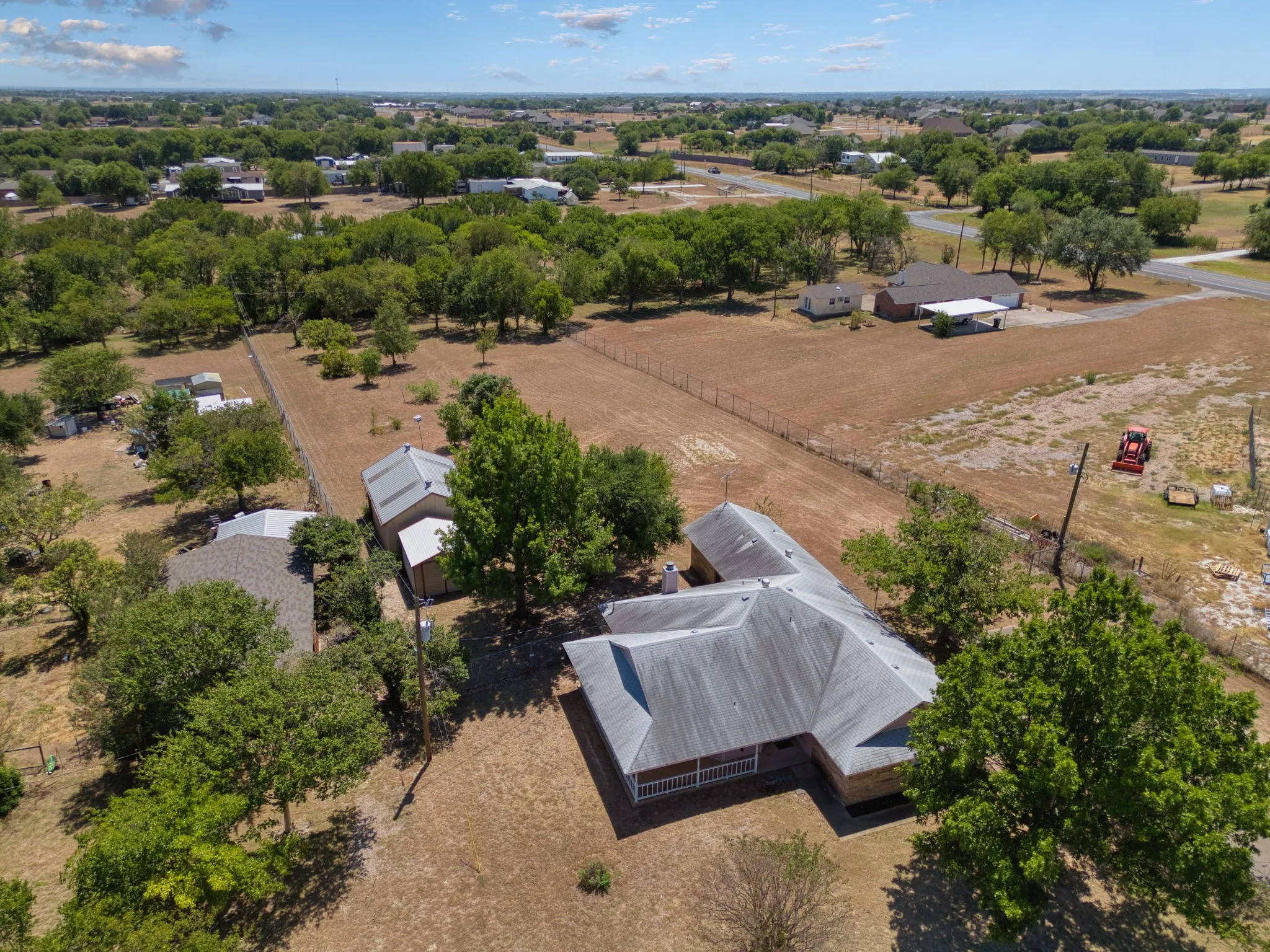 Expansive lot with mature trees, multiple outbuildings, and a main residence featuring a covered front porch and a multi-pitched roof