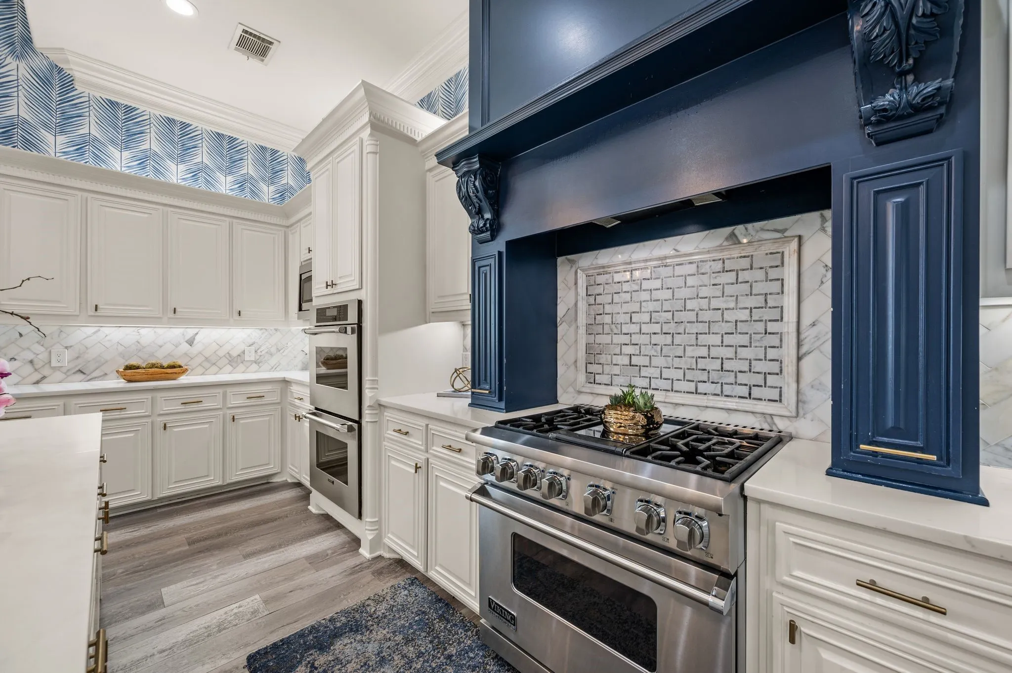 Gourmet kitchen featuring a stainless steel gas range, custom navy range hood with intricate corbels, white perimeter cabinetry, stone countertops, and a marble tile backsplash
