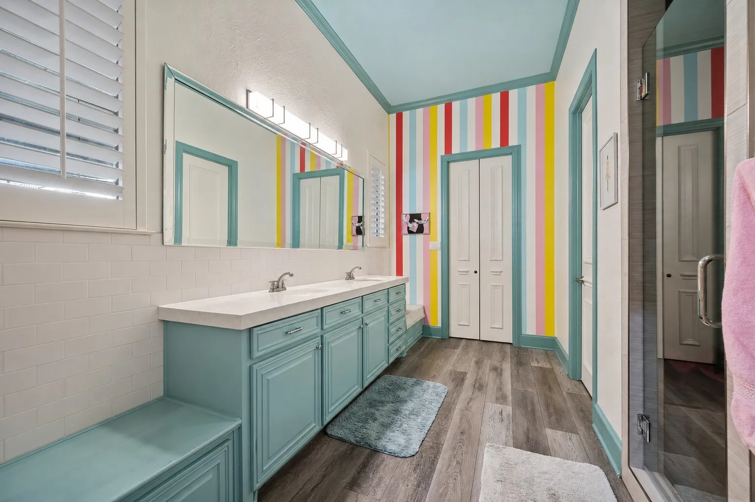 Bathroom featuring a dual vanity with light blue cabinetry and integrated sinks, a full-width mirror with overhead bar lighting, and a walk-in shower with a glass enclosure