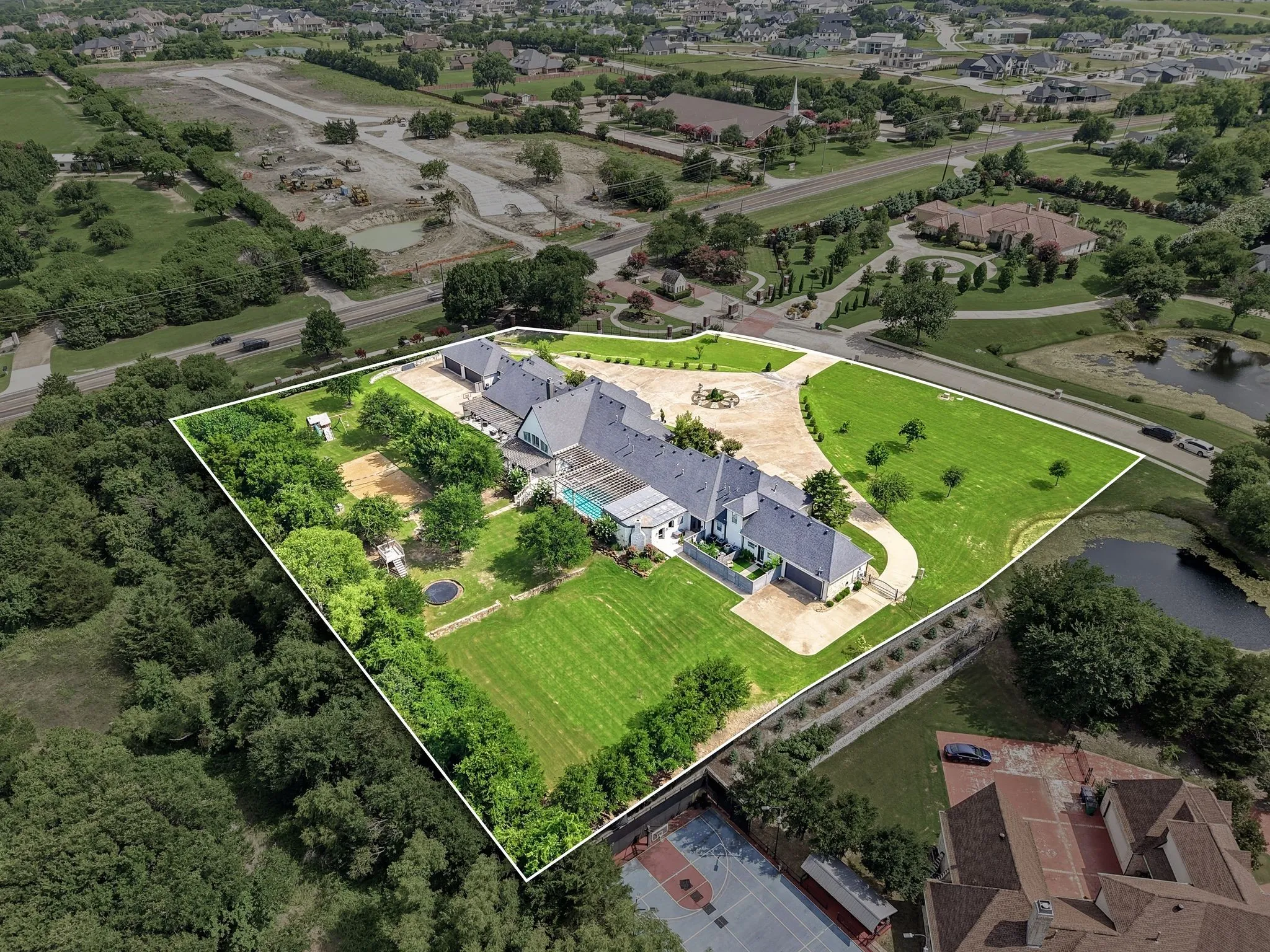 Expansive property featuring a large residence with a multi-car garage, extensive paved driveways, a swimming pool, and mature trees