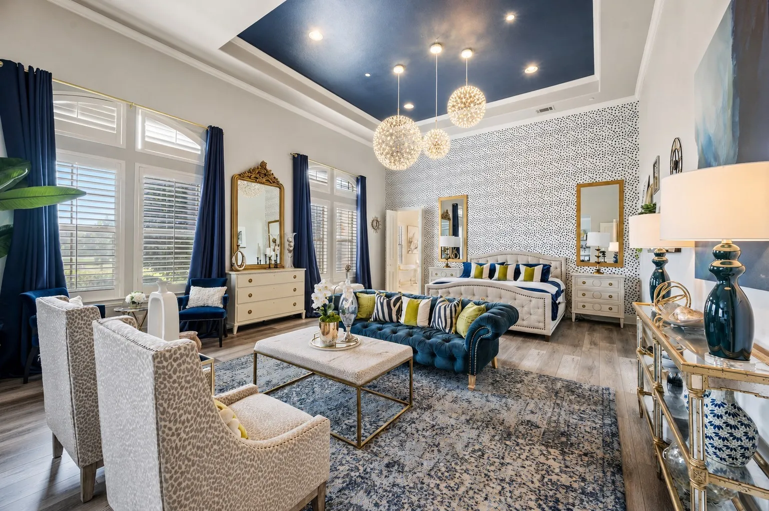 Spacious interior featuring a stepped tray ceiling with recessed lighting, multiple pendant light fixtures, wood-finish flooring, and expansive windows with plantation shutters