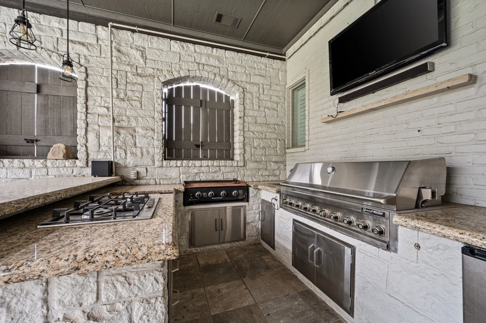 Outdoor kitchen featuring stone-clad walls, granite countertops, a built-in gas cooktop, a large stainless steel grill, and integrated stainless steel cabinetry