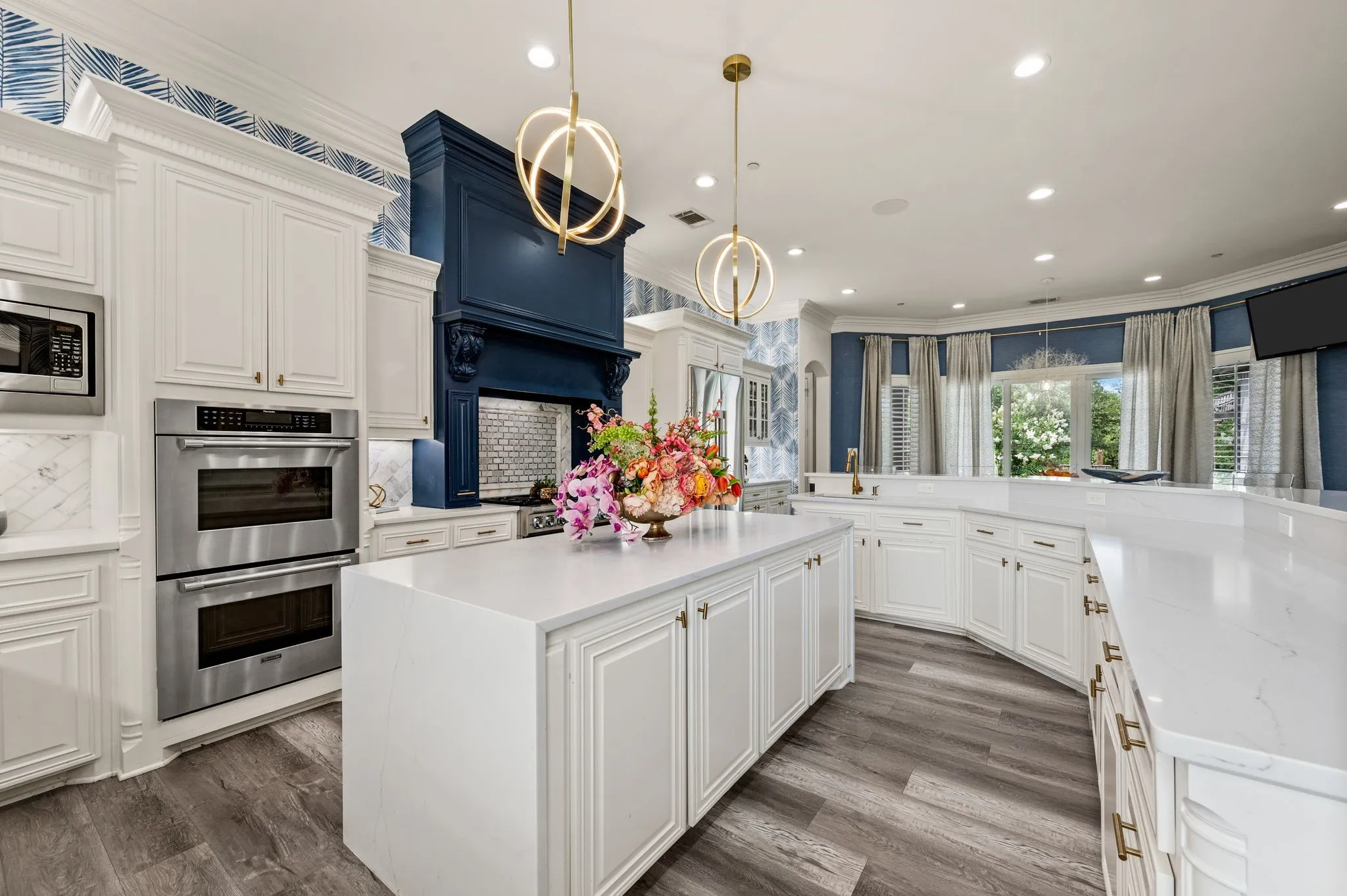 Gourmet kitchen featuring a substantial island, double wall ovens, a distinctive blue range hood, white cabinetry, and wood-finish flooring