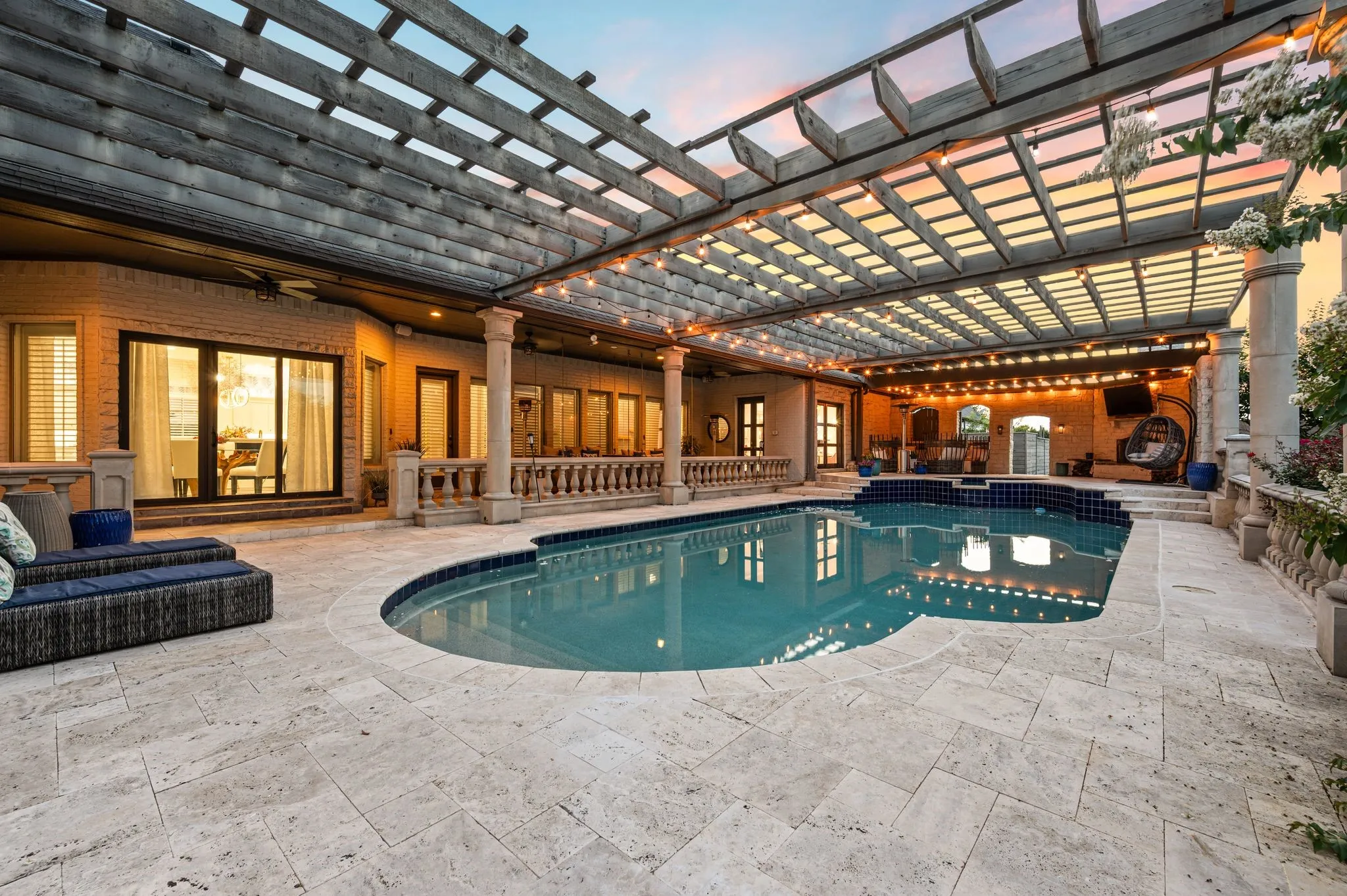 Outdoor oasis featuring a freeform pool with integrated steps, an expansive paver patio, a large pergola, and string lighting