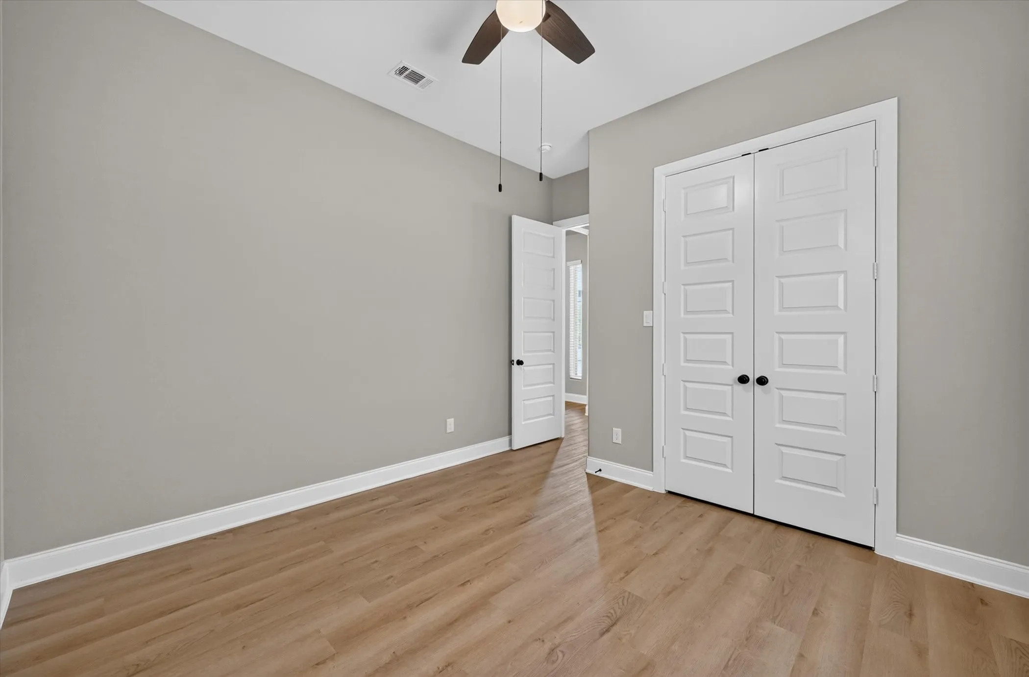 Neutral wall color, wood-finish flooring, white paneled double doors with matte black hardware, and a ceiling fan