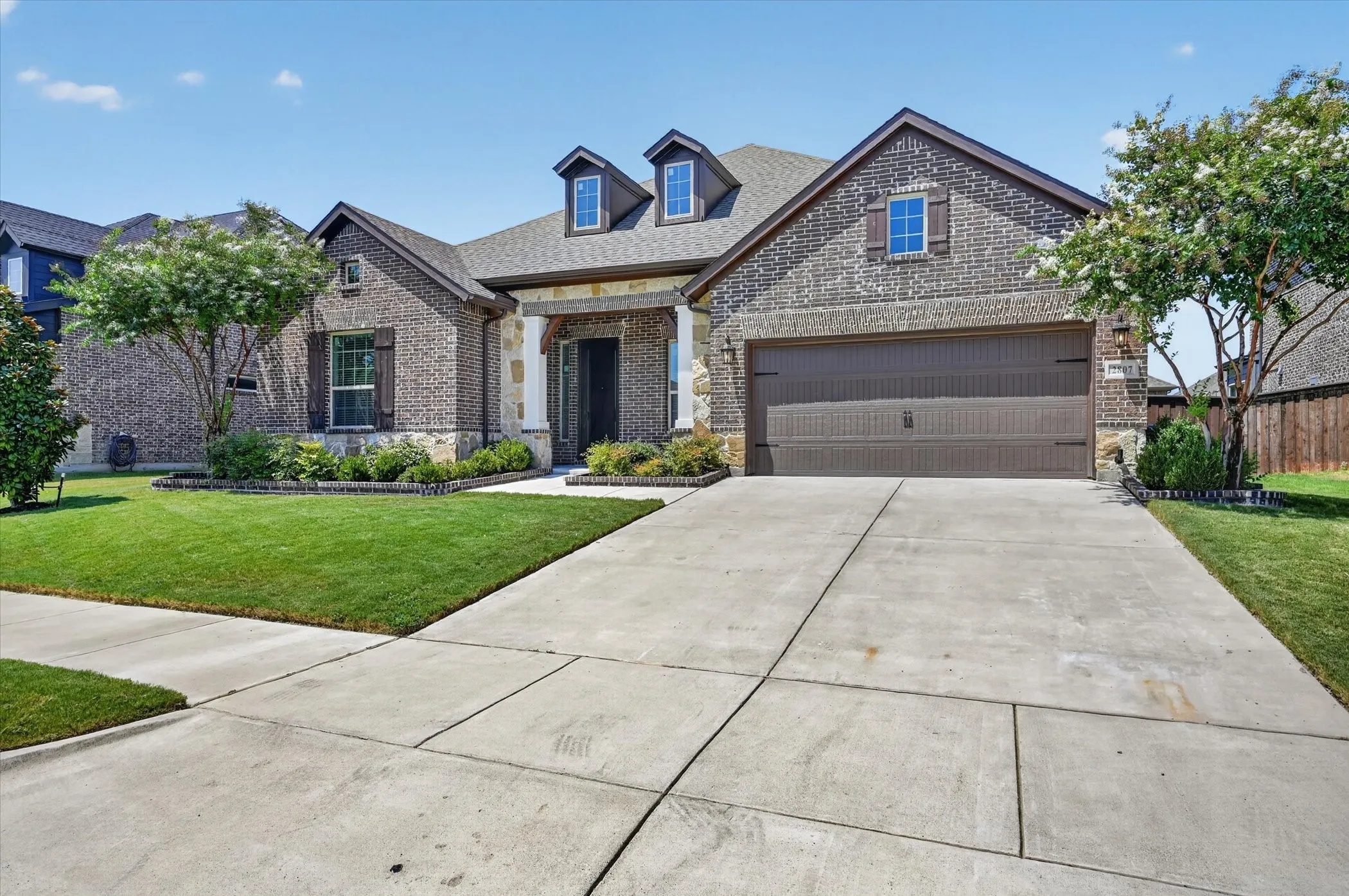 Brick exterior with stone accents, two-car garage, dormer windows, covered entry, and a concrete driveway