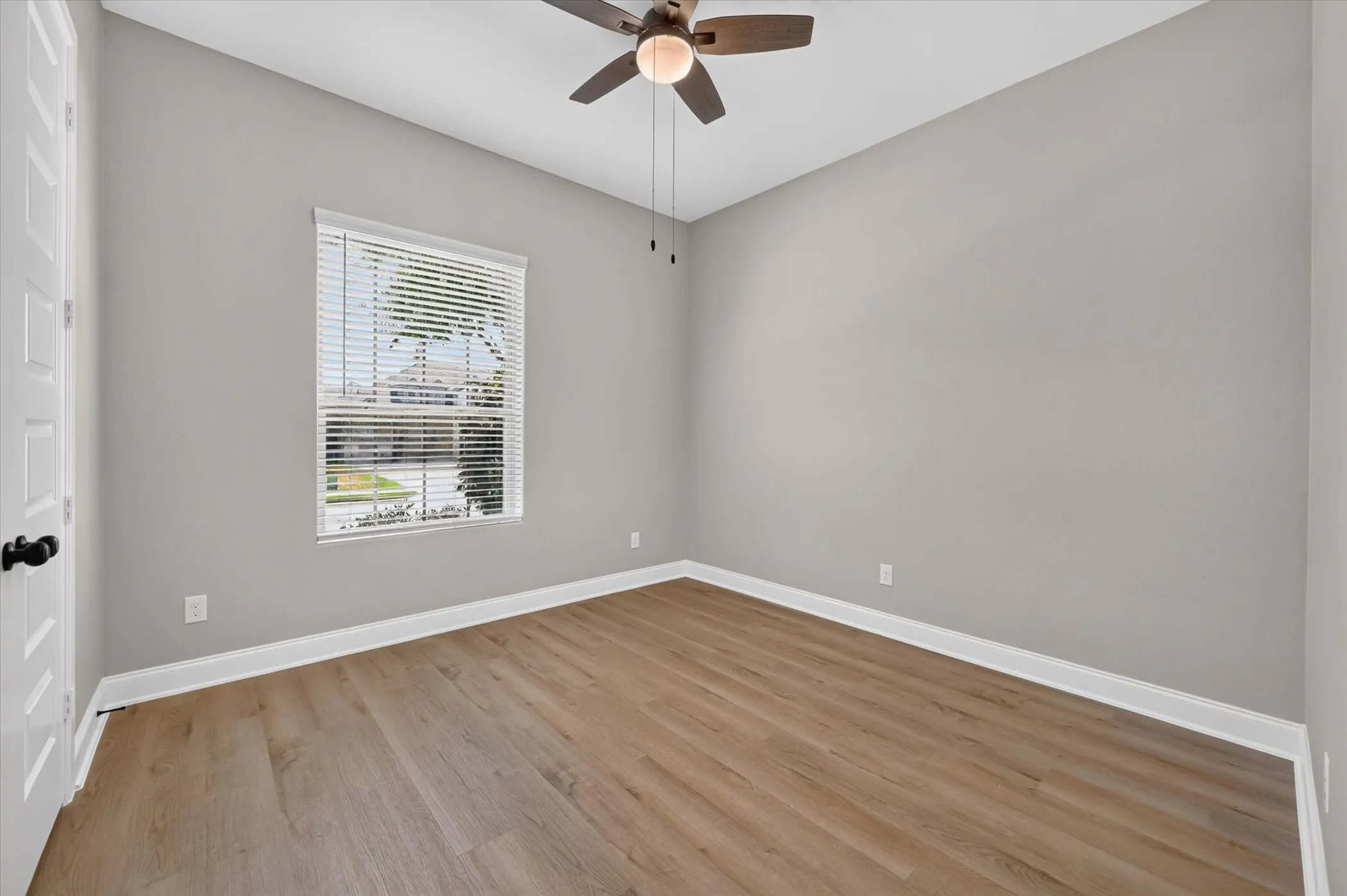 Recessed window with horizontal blinds, wood-finish flooring, ceiling fan with light fixture, and white trim