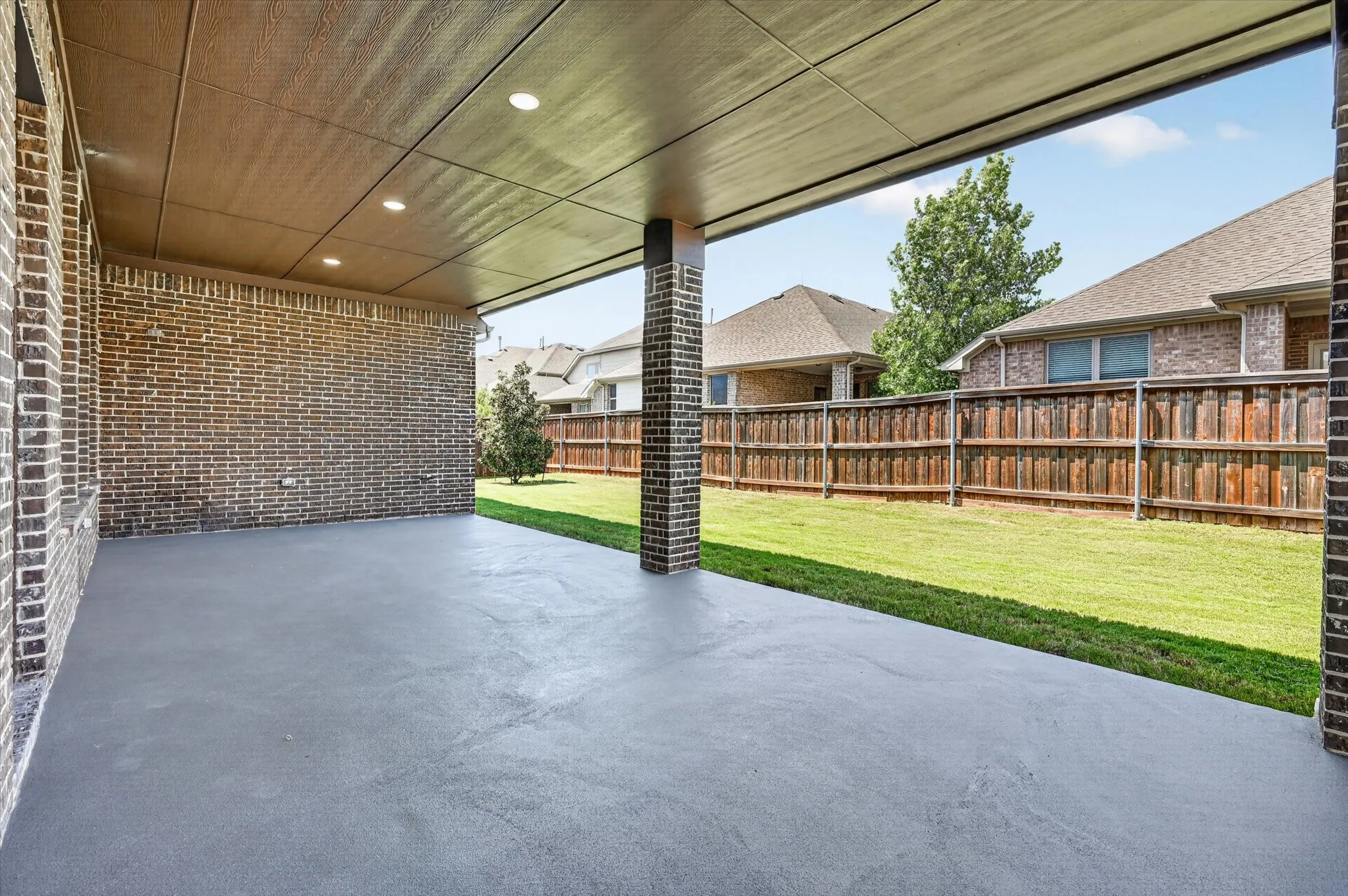 Covered patio with recessed lighting, brick-clad walls and support column, and concrete flooring
