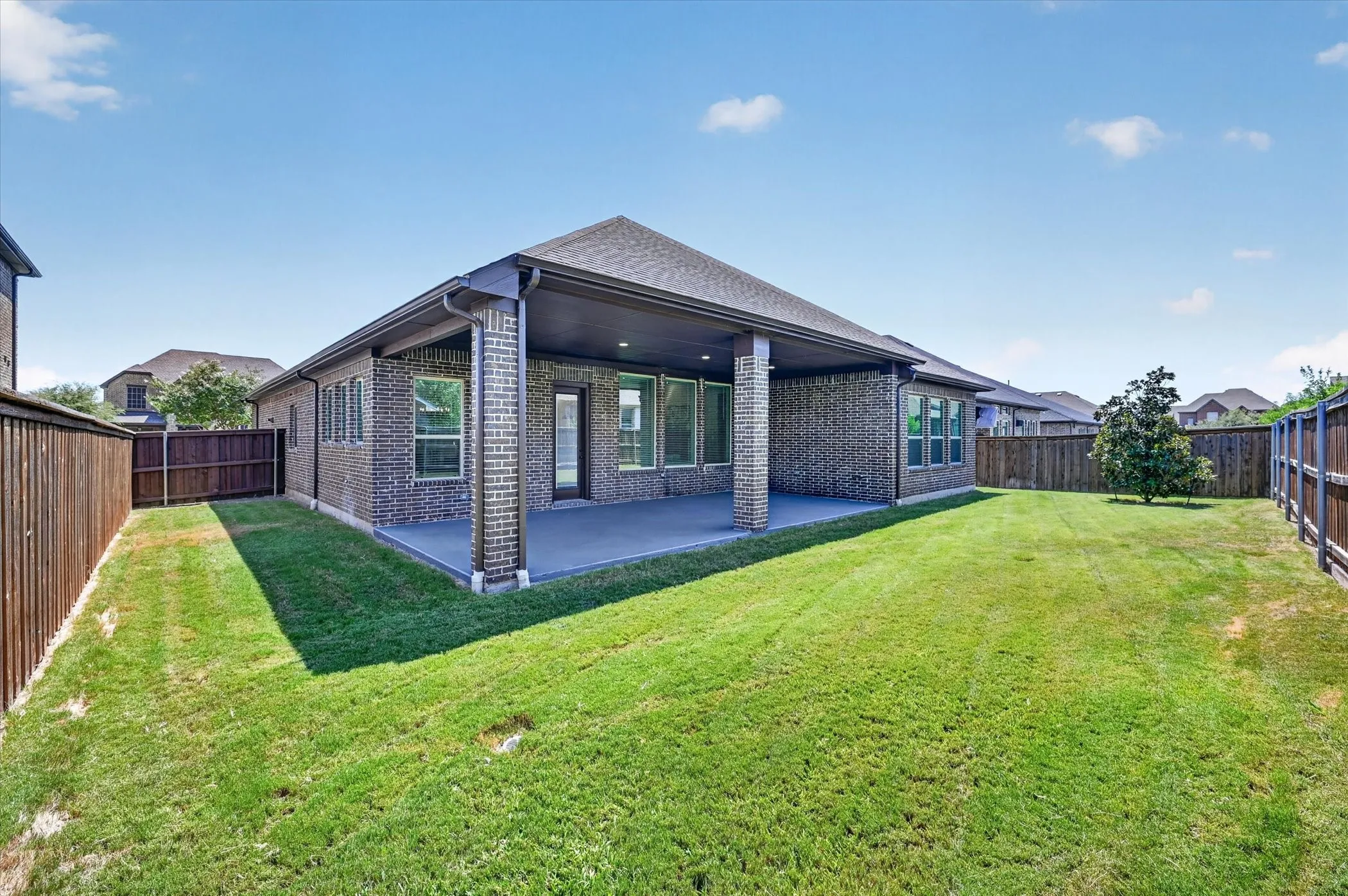 Expansive backyard featuring a covered patio, brick exterior, and wood fencing