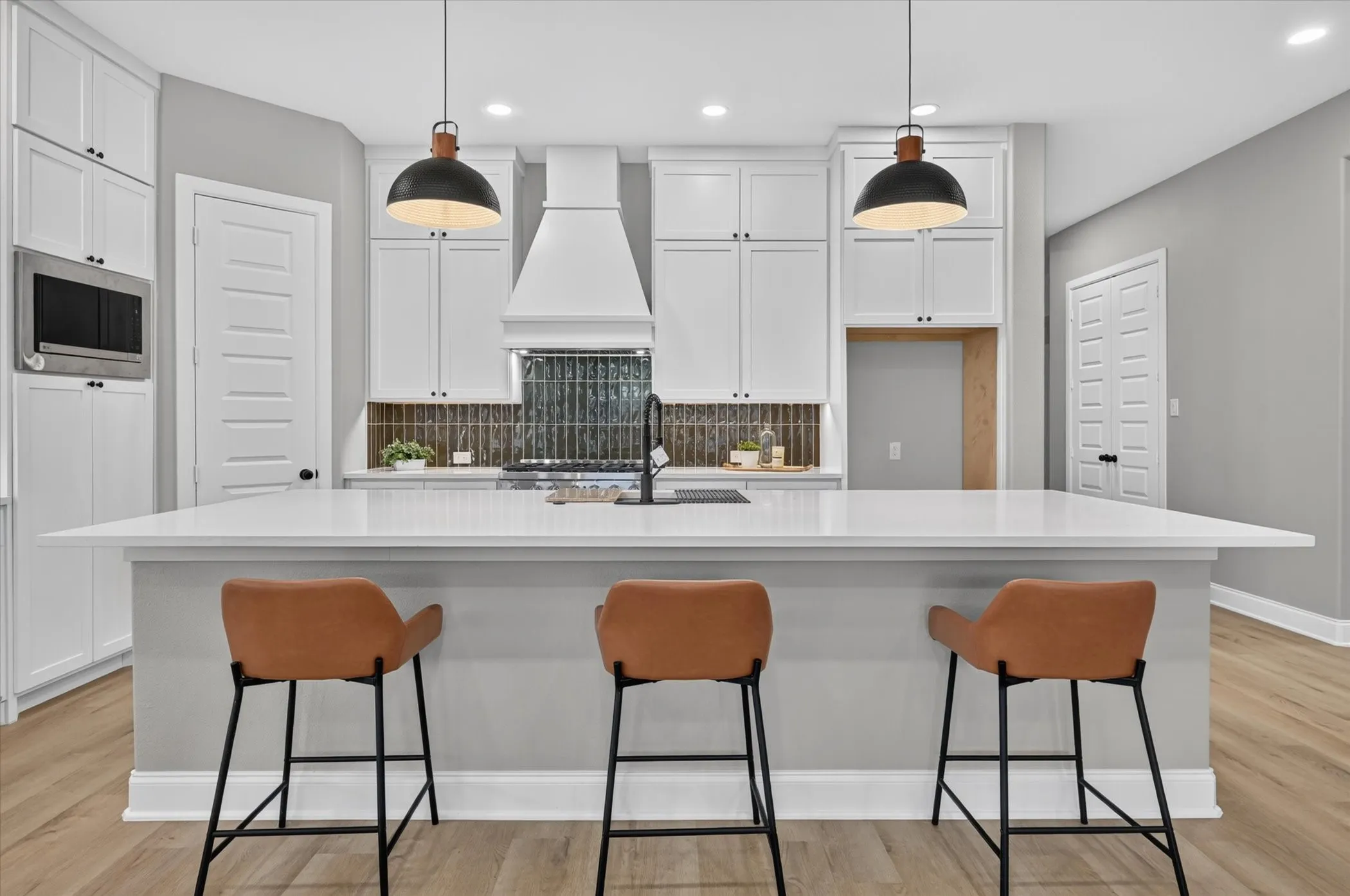White shaker cabinetry with black hardware, wood-finish flooring, a stainless steel microwave, a decorative range hood, and pendant lighting