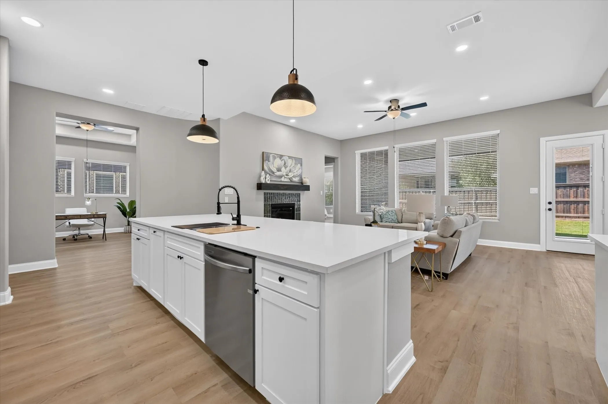 Kitchen island with a built-in sink and stainless steel dishwasher, white shaker cabinetry, wood-finish flooring, recessed lighting, and a fireplace with a dark tile surround