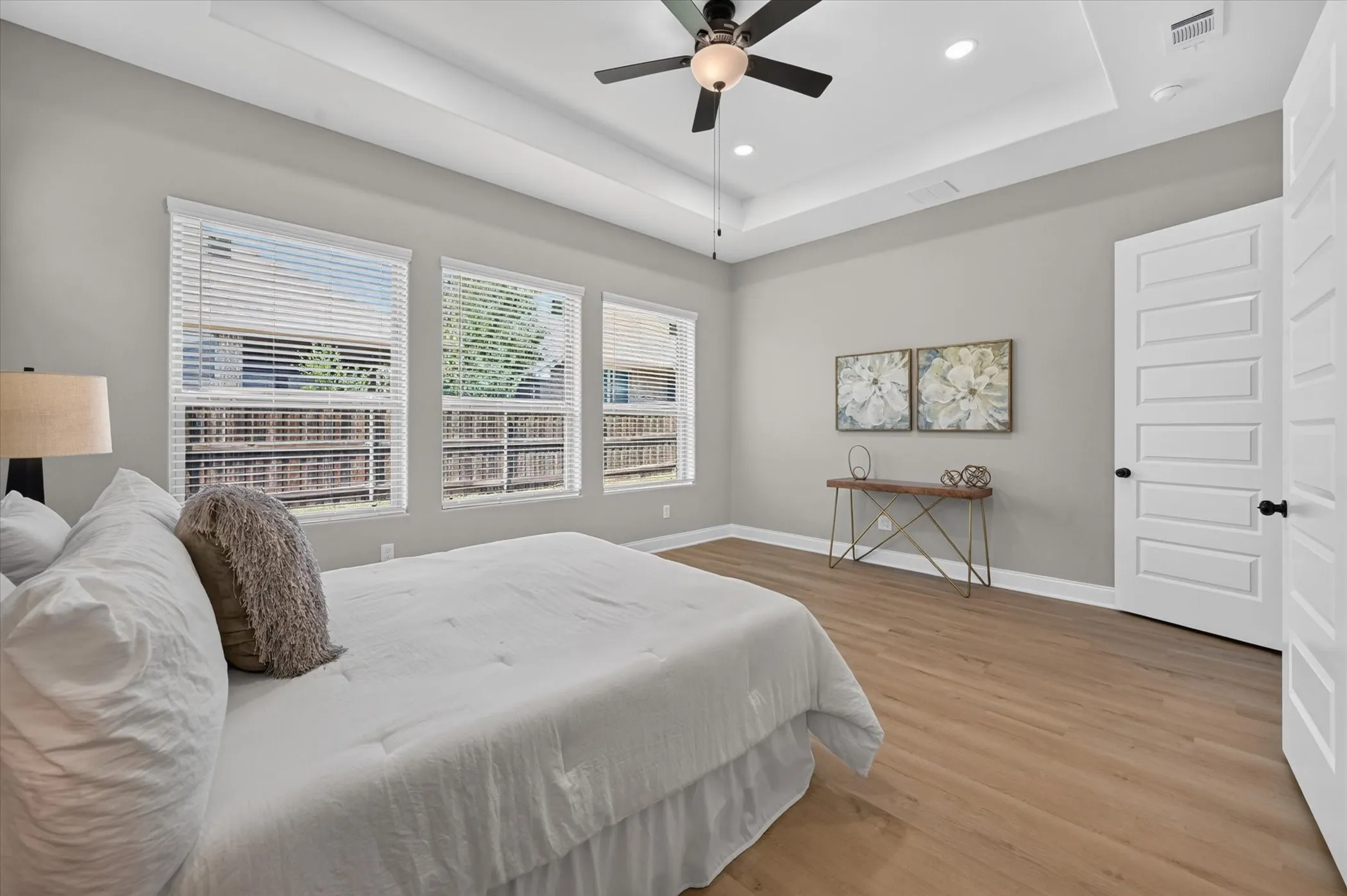 Recessed lighting, wood-finish flooring, tray ceiling, ceiling fan, and multiple windows with blinds