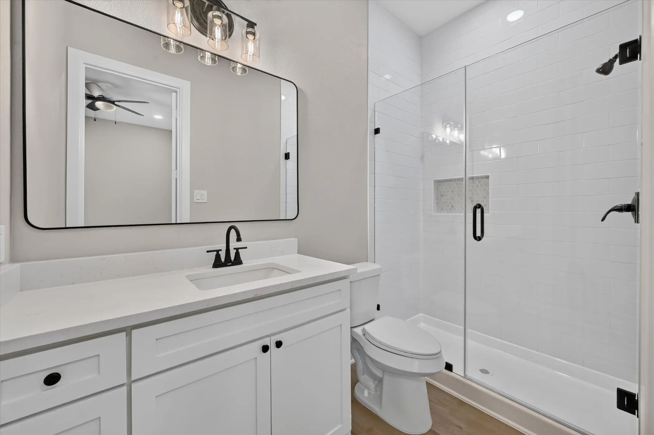 Bathroom featuring a glass-enclosed shower, subway tile surround, built-in shower niche, white vanity with integrated sink, and wood-finish flooring