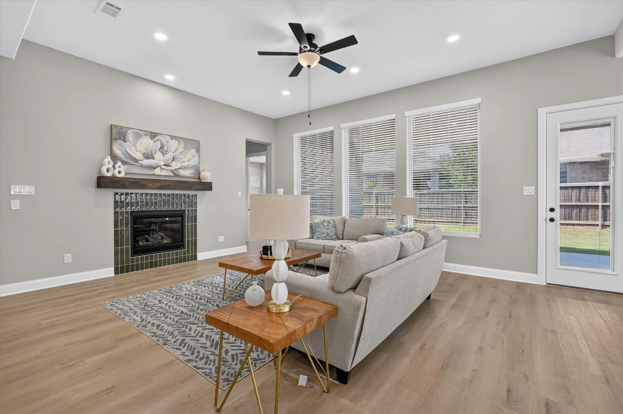 Wood-finish flooring throughout, ceiling fan with integrated lighting, recessed lighting, fireplace with a tiled surround and wood mantel, and multiple windows