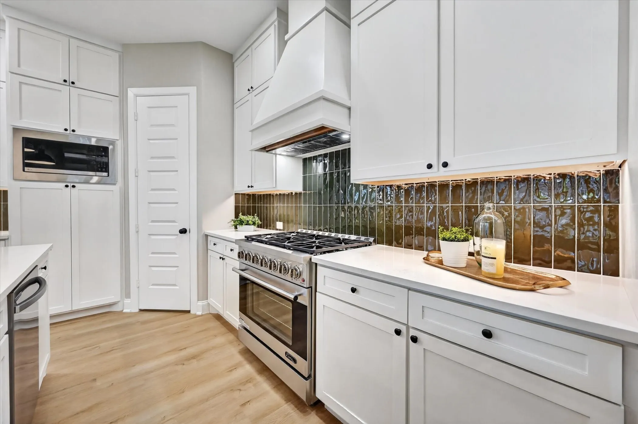 White cabinetry, stainless steel range, white countertops, textured dark green tile backsplash, and wood-finish flooring