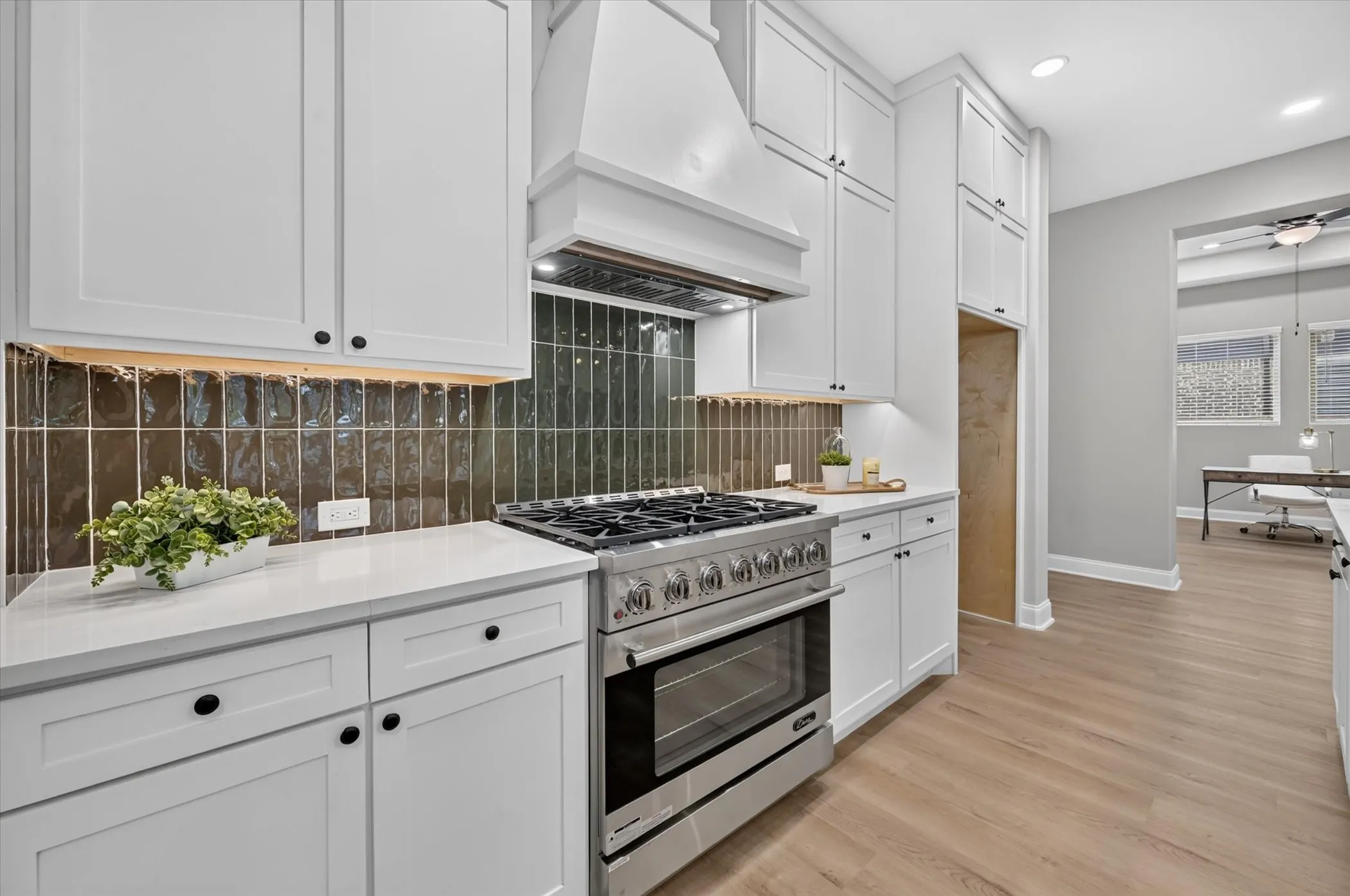 White shaker cabinetry with black hardware, stainless steel range, white stone countertops, and wood-finish flooring