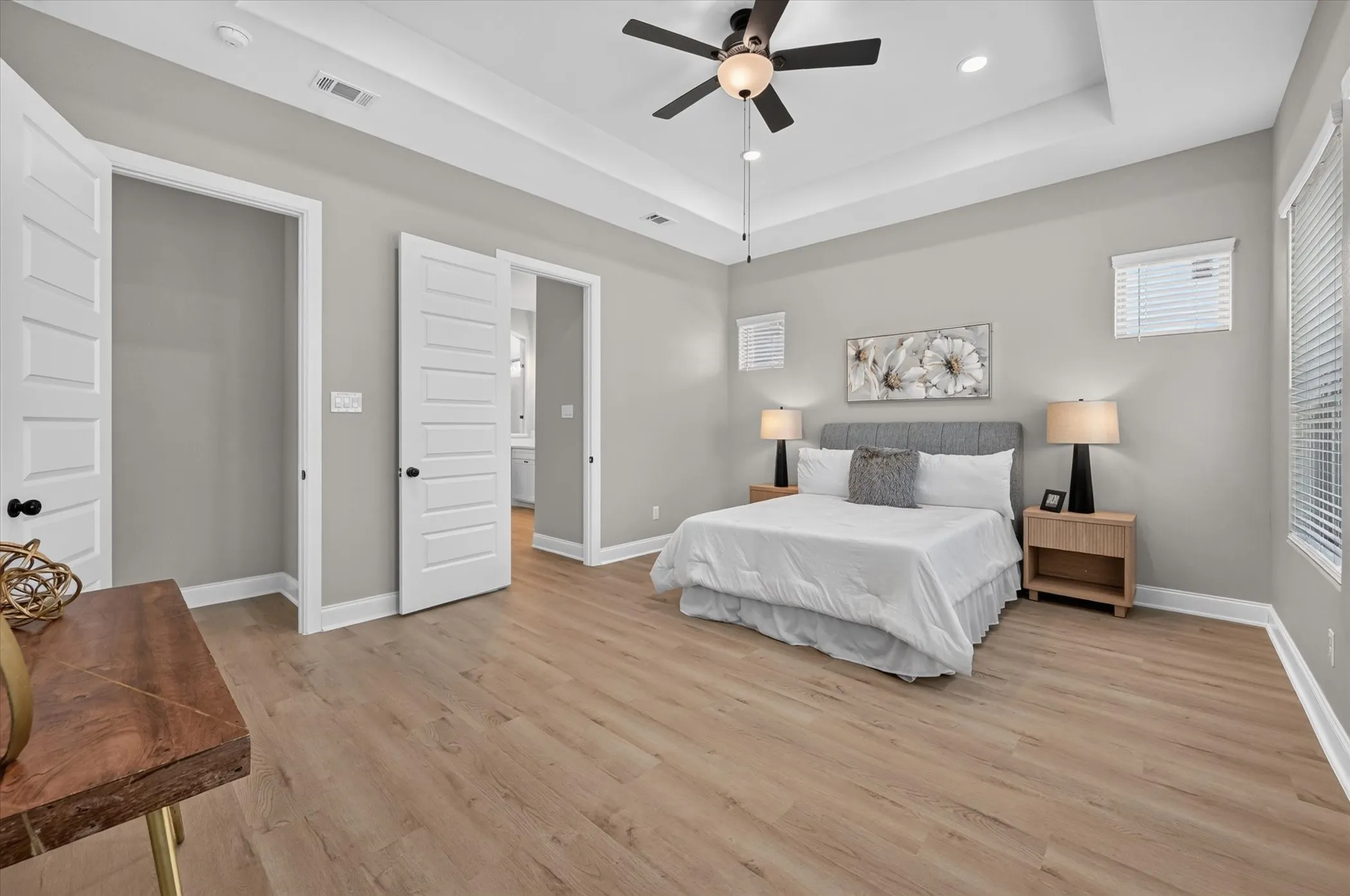 Tray ceiling with recessed lighting, wood-finish flooring, ceiling fan, and multiple windows with blinds