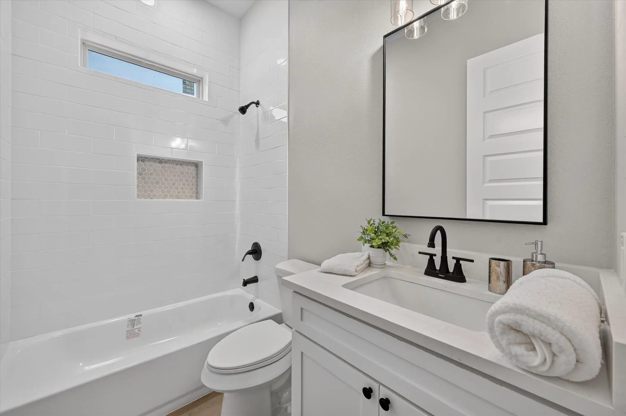 White subway tile surround with integrated niche, modern rectangular vanity mirror, white flat-panel vanity cabinetry, black matte fixtures, and an elongated window