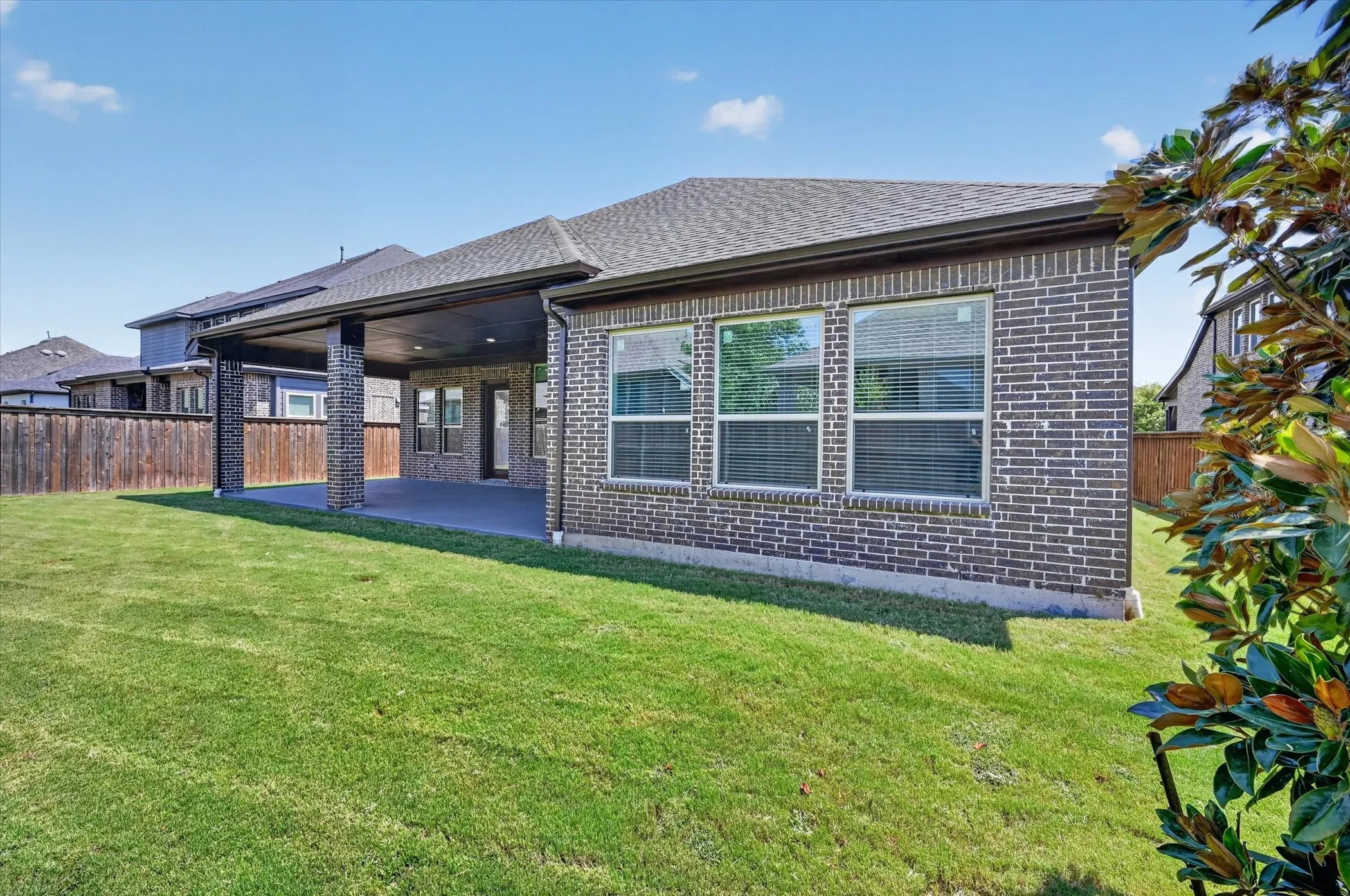 Expansive backyard featuring a covered patio, brick exterior, multiple windows, and a wood privacy fence