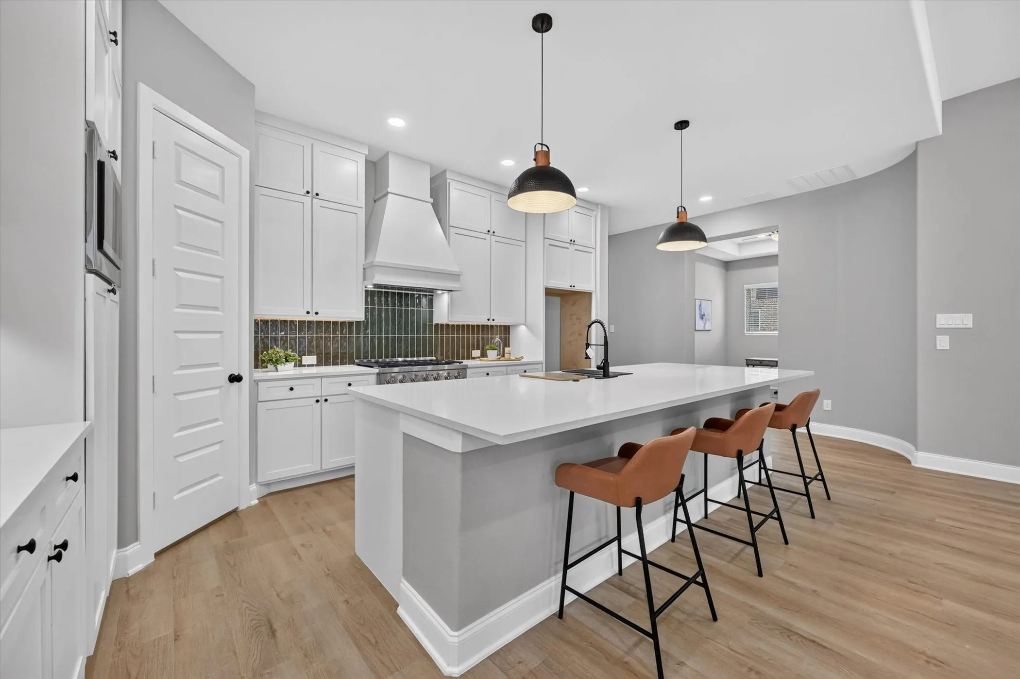 White cabinetry with black hardware, wood-finish flooring, white countertop island, pendant lighting, and tiled backsplash