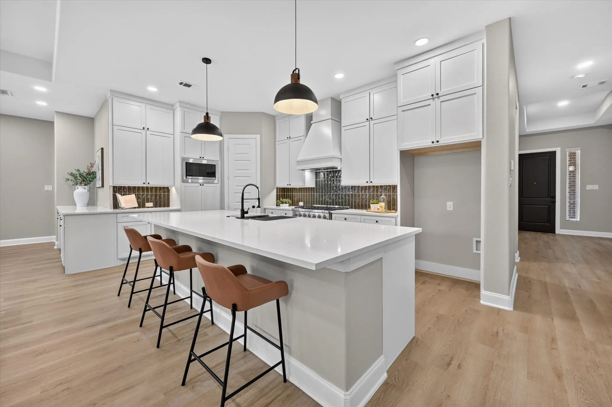 Kitchen featuring a substantial island with countertop seating, white shaker-style cabinetry, dark tile backsplash, and wood-finish flooring