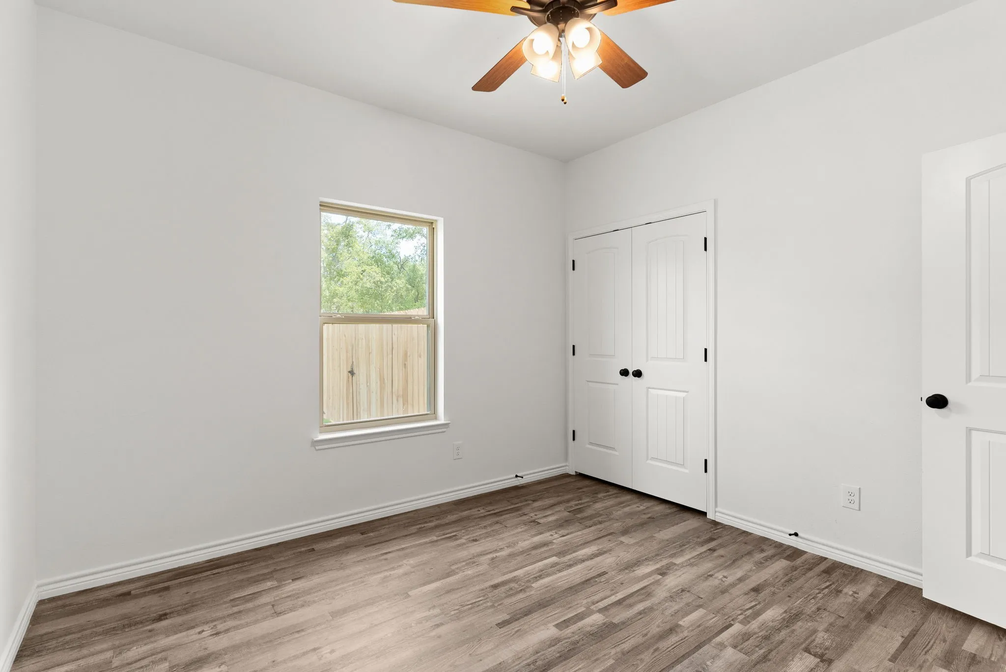 Wood-finish flooring, white paneled doors, ceiling fan with integrated lighting, and a double-pane window