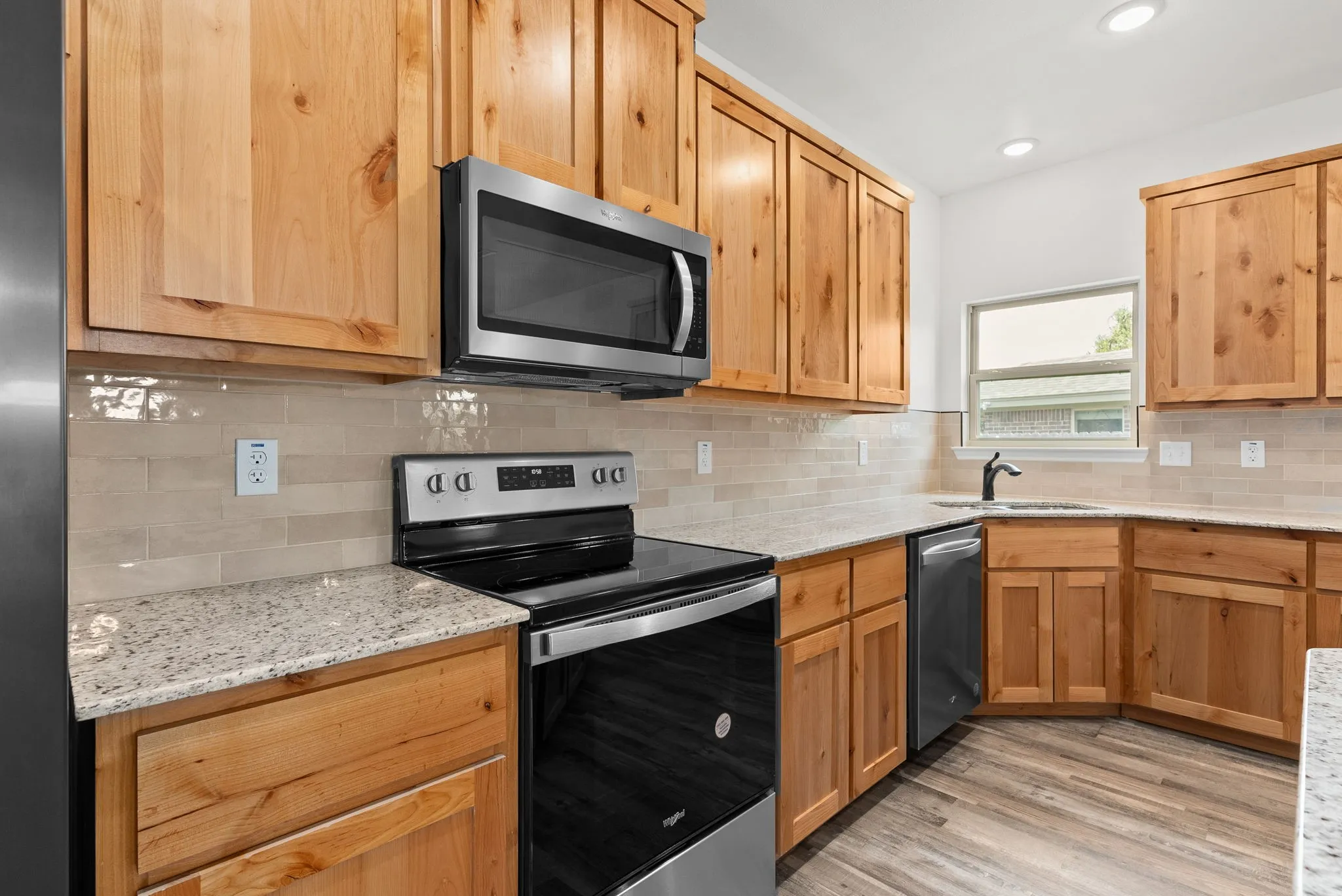 Kitchen featuring wood cabinetry, light-toned stone-finish countertops, stainless steel appliances, a tile backsplash, and wood-finish flooring