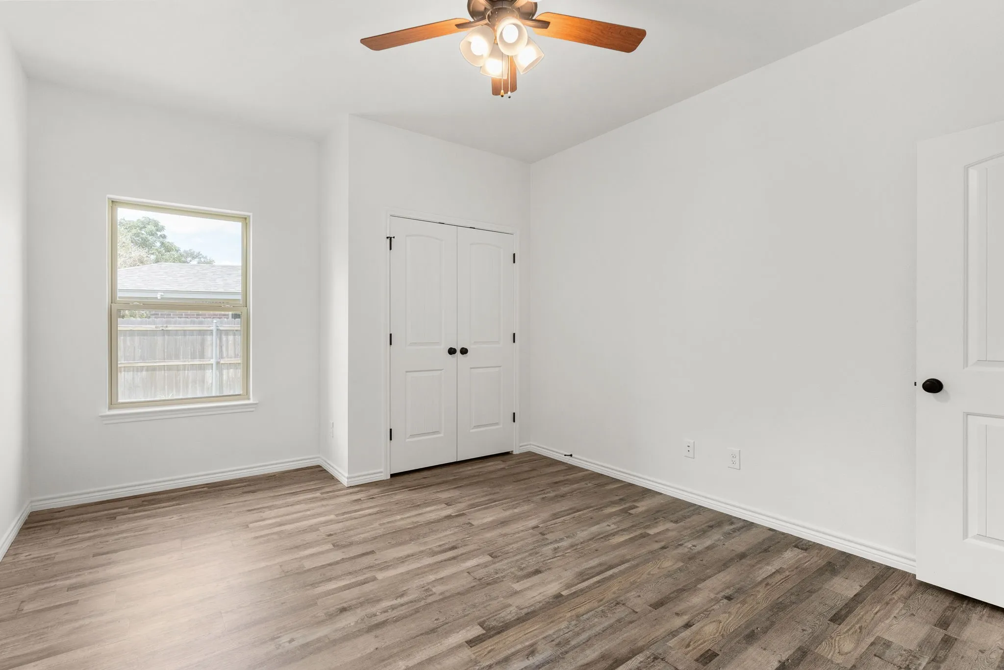 Wood-finish flooring, white walls, and a ceiling fan with integrated lighting