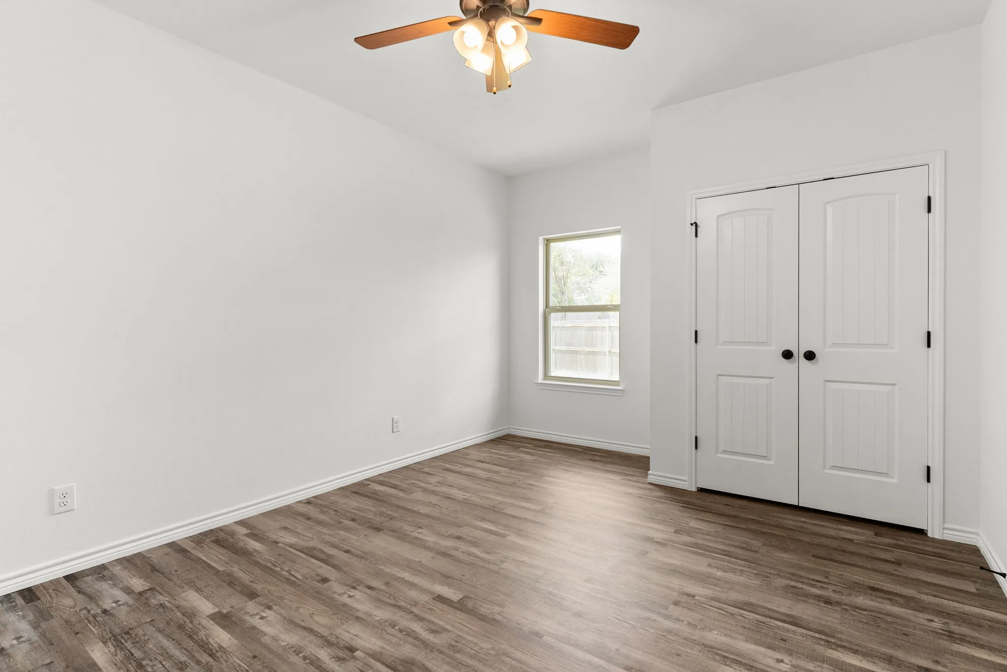 Wood-finish flooring, white walls, double-door closet with black hardware, ceiling fan with integrated lighting, and a single window