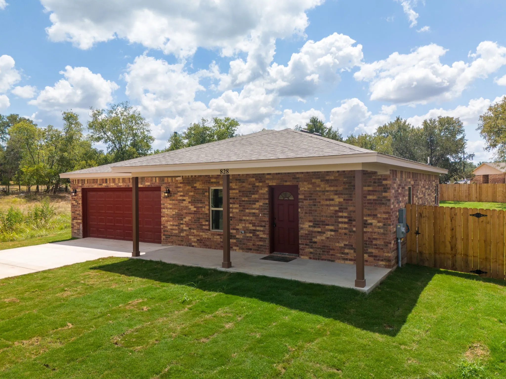 Brick exterior with a covered porch, attached garage, concrete driveway, and wood fence