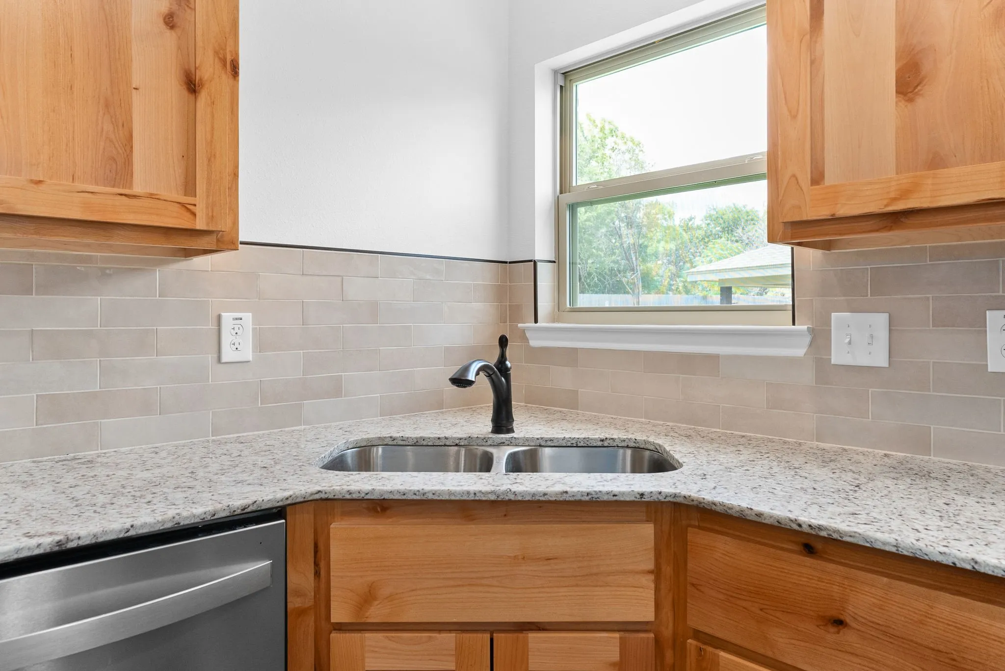Corner kitchen sink with a double basin and matte black faucet, set in a light granite countertop