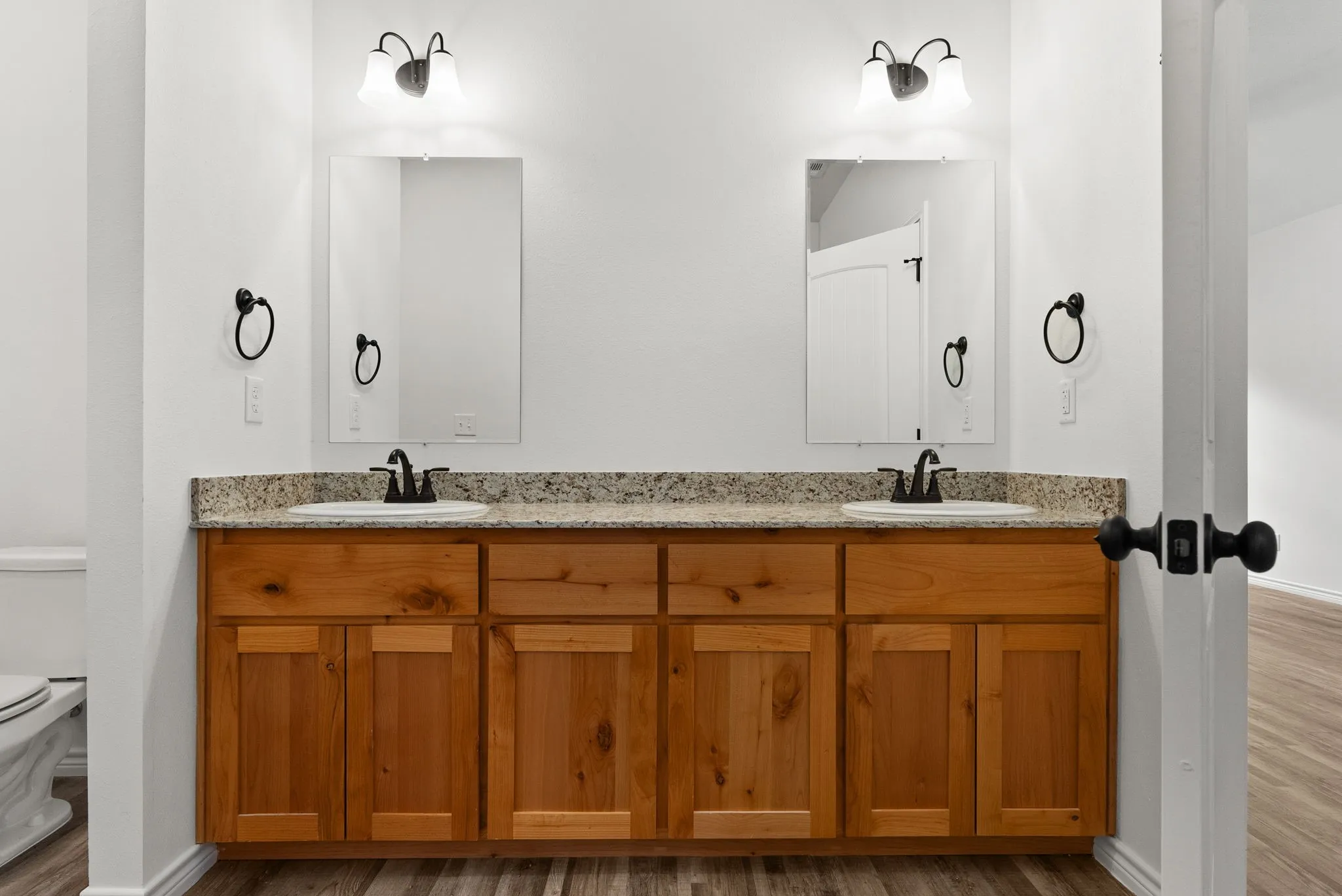 Dual sink vanity with wood-finish cabinetry, speckled countertop, and individual mirrors