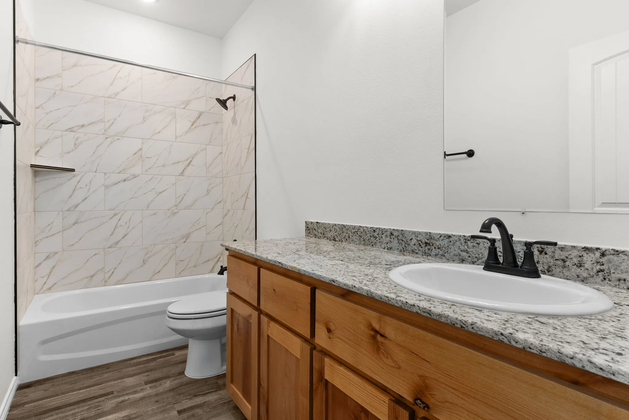 Tub and shower combination with tile surround, wood-finish flooring, wood vanity cabinetry, and a countertop with an integrated sink
