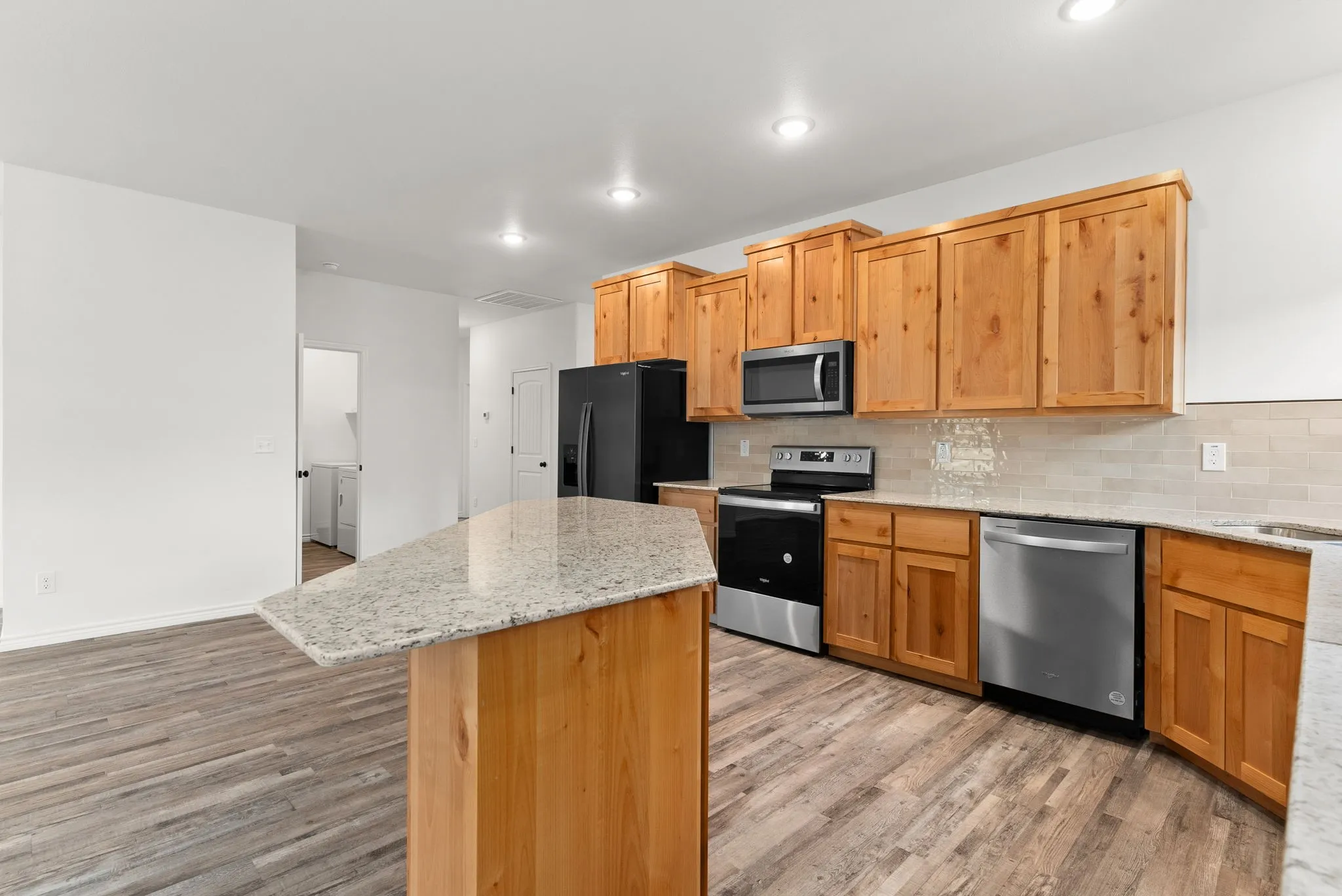 Kitchen featuring wood-finish cabinetry, stainless steel appliances, granite-style countertops, a tile backsplash, and wood-finish flooring