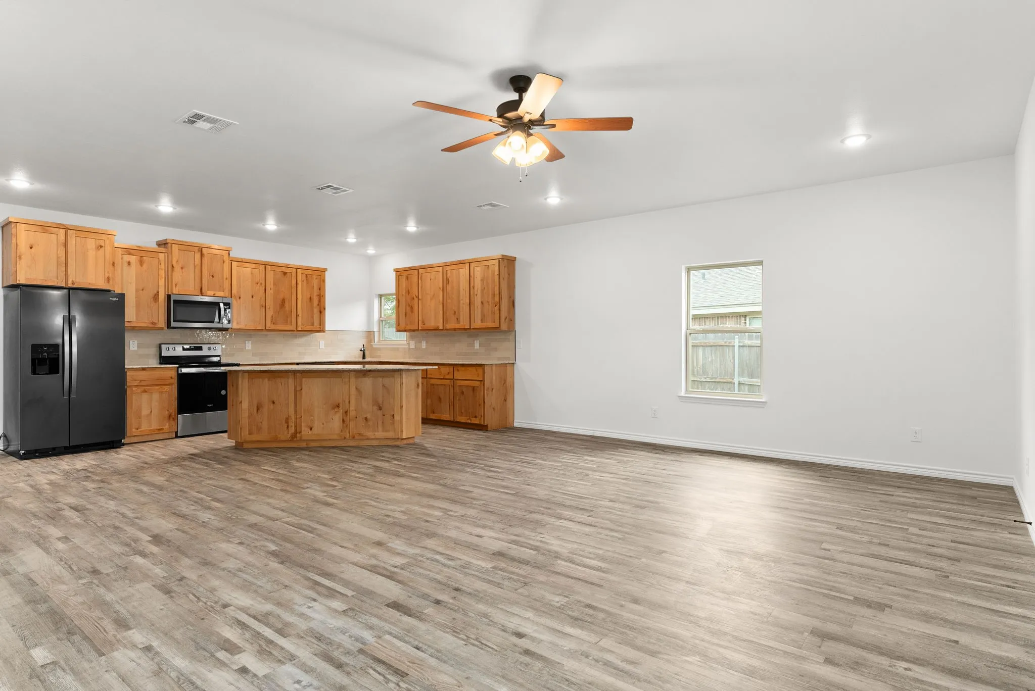 Open-concept living area with wood-finish flooring, a ceiling fan, and recessed lighting
