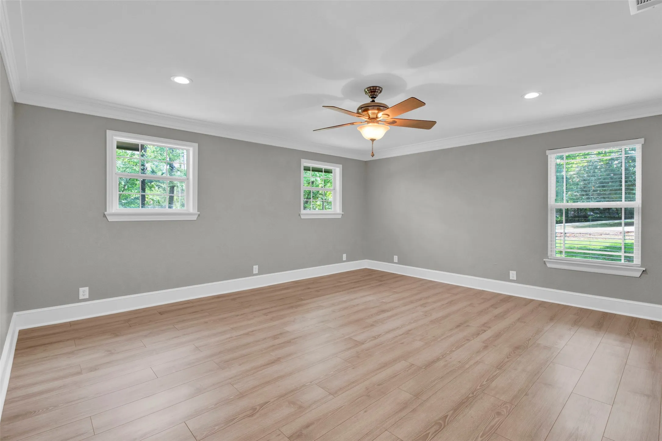 Spacious room featuring wood-finish flooring, white crown molding, recessed lighting, and a ceiling fan